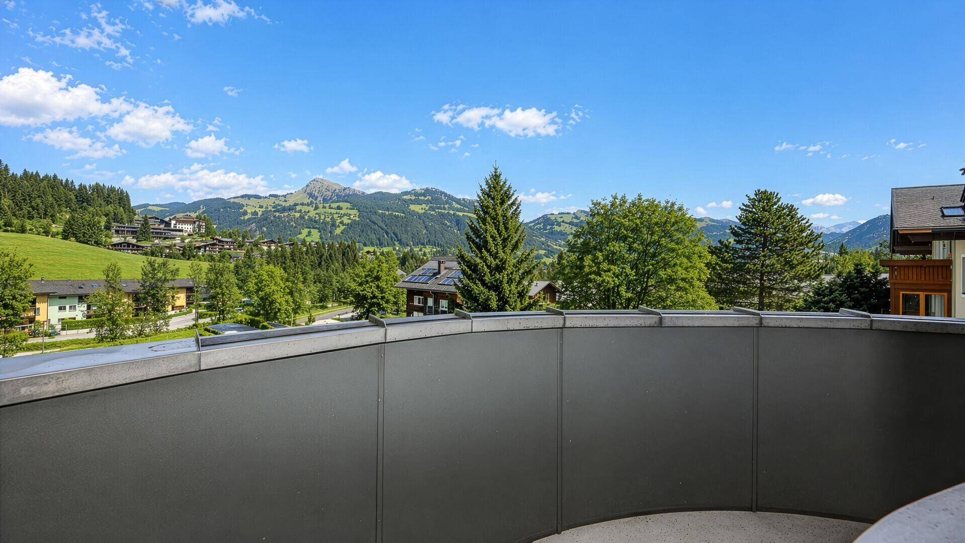 Balkon mit weitem Blick auf die grüne Berglandschaft und umliegende Häuser.