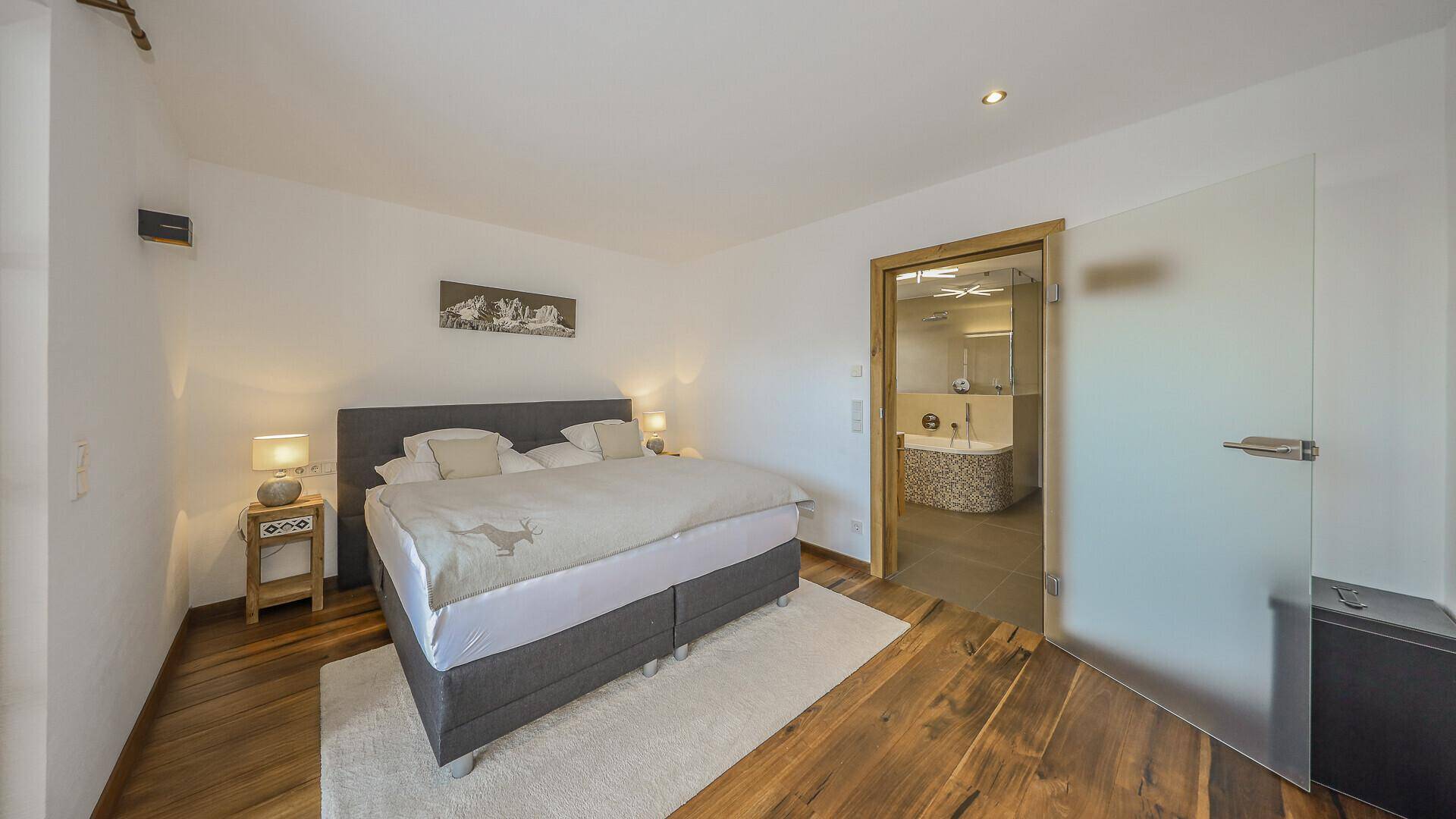 Schlafzimmer mit Holzboden und direktem Zugang zu einem modernen Badezimmer.