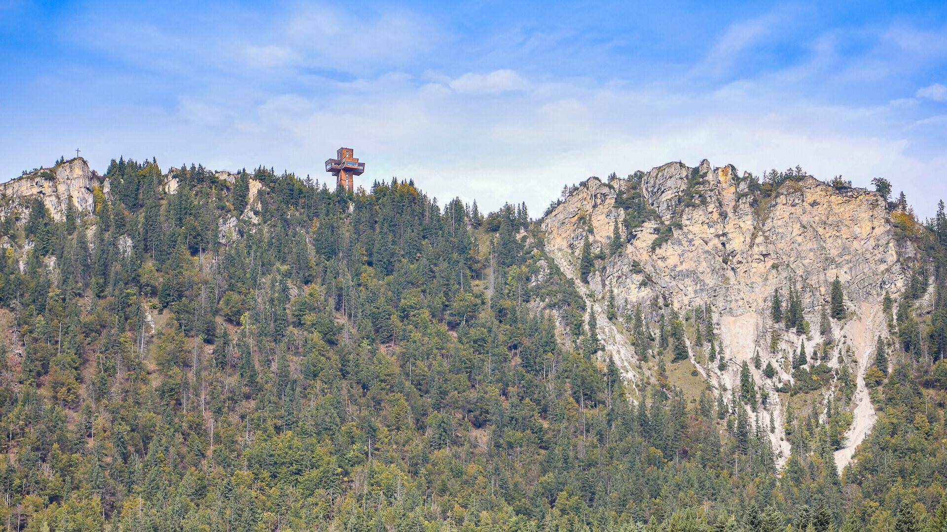 Bewaldeter Berg mit einem Aussichtsturm auf dem Gipfel unter einem weiten blauen Himmel.