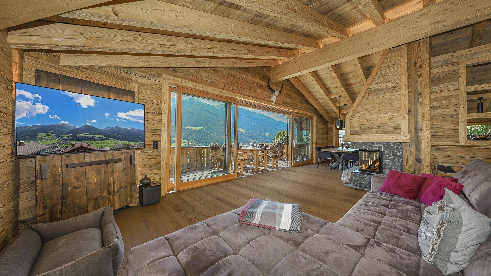 Rustikales Wohnzimmer mit Holzwänden, bequemer Couch und Zugang zum Balkon mit Bergblick.