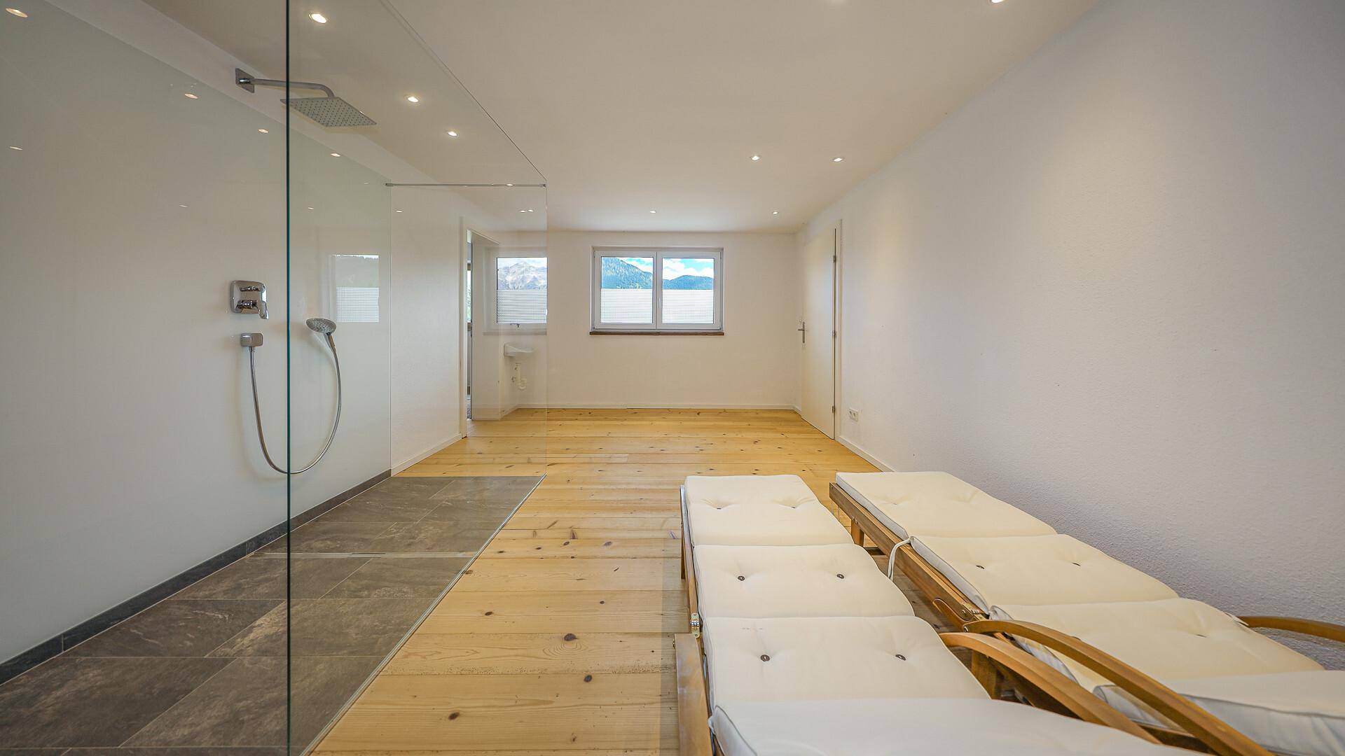 Heller Wellnessbereich mit Liegestühlen, Dusche und Fenster mit Bergblick.