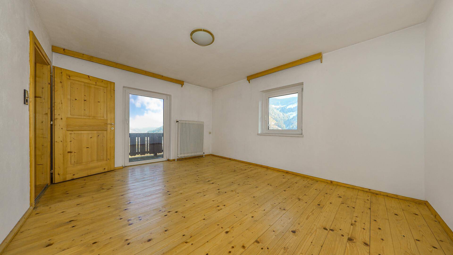 Schlafzimmer mit Holzdielenboden, weiß gestrichenen Wänden und Zugang zu einem Balkon mit Bergblick.