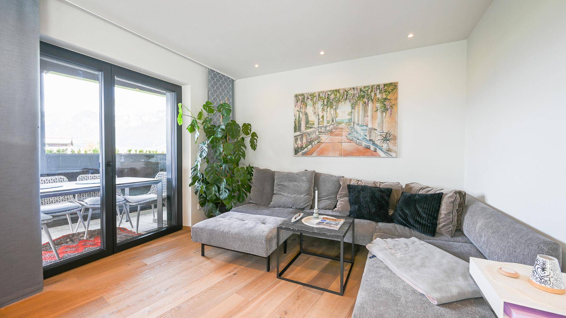 Gemütliches Wohnzimmer mit großem Ecksofa, Holzboden und Zugang zu einem Balkon oder Terrasse.