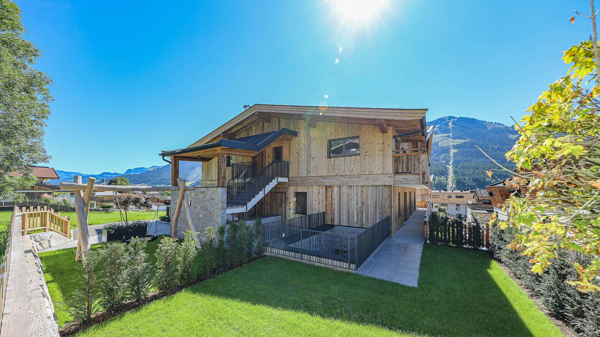 Modernes Mehrfamilienhaus im alpinen Stil mit Garten, Spielplatz und Bergblick.