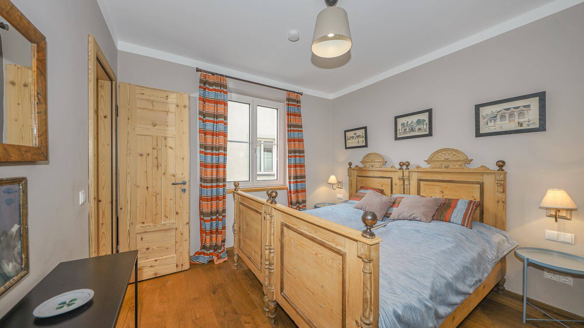 Traditionelles Schlafzimmer mit Holzbett, Holzboden und farbenfrohen Vorhängen.