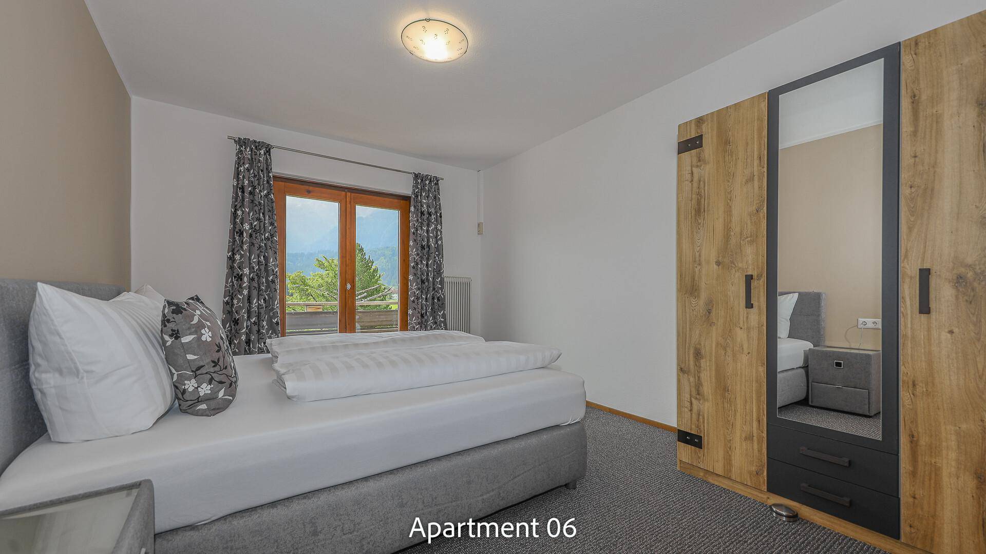 Schlafzimmer von Apartment 06 mit Doppelbett, Holzschrank mit Spiegel und Teppichboden, mit Balkonzugang.