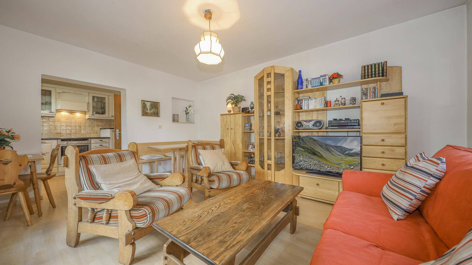 Gemütliches Wohn-Esszimmer mit traditionellen Holzmöbeln und Blick in die Küche.