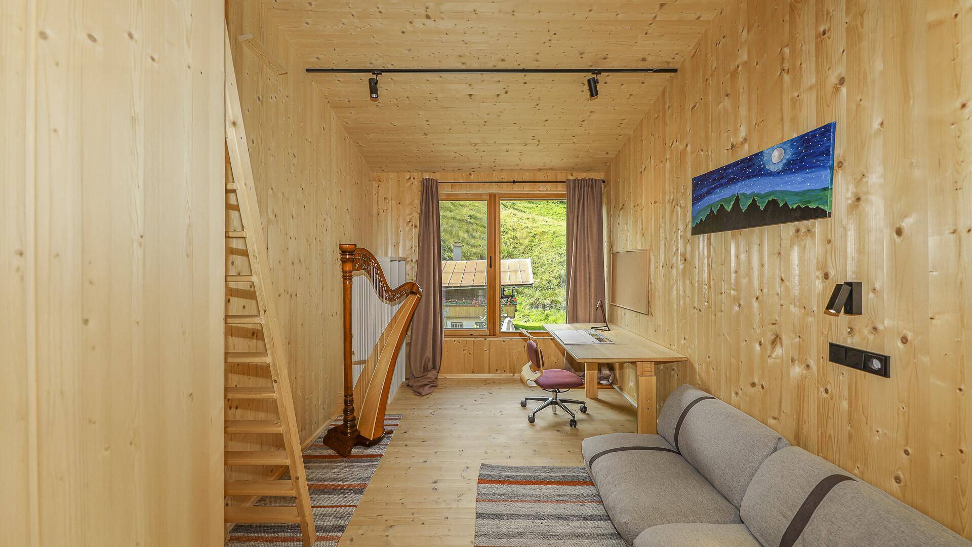 Gemütlicher Wohnbereich mit Sofa, Holzwänden und einem Fenster mit Blick ins Grüne.