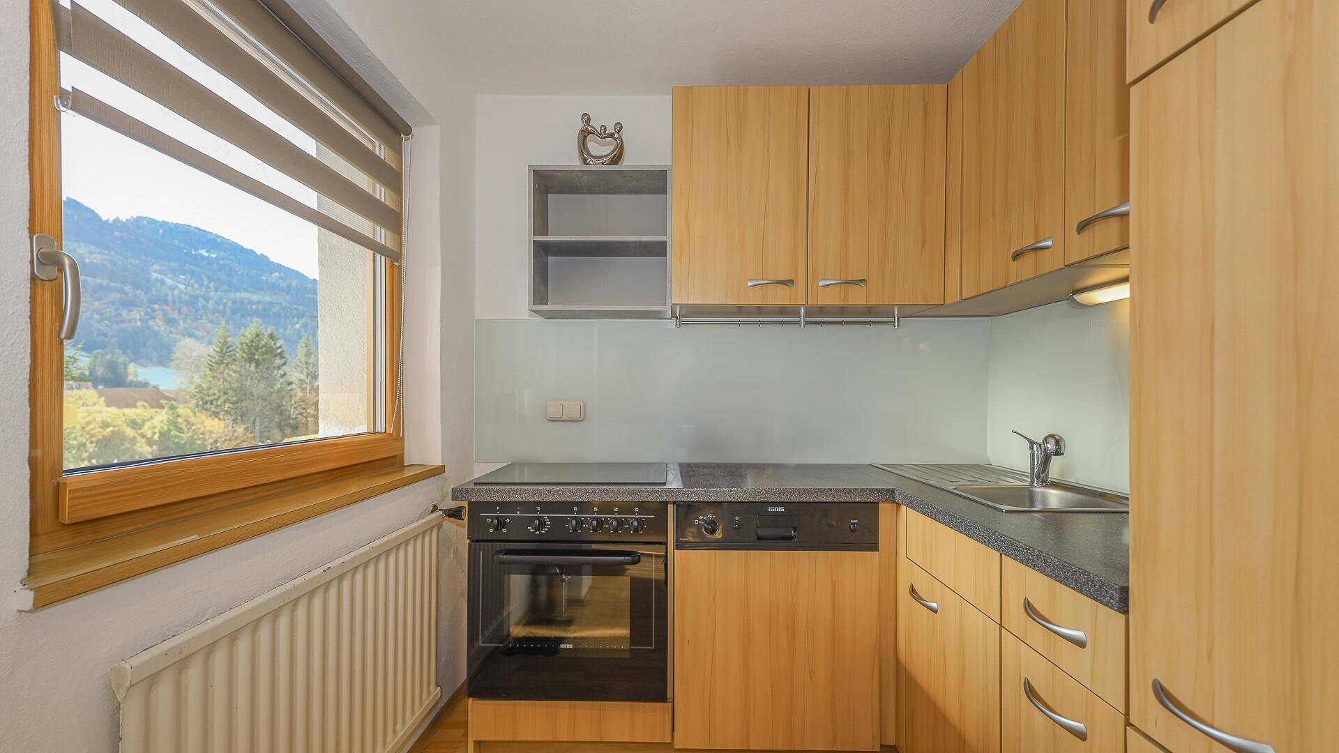 Kleine Küche mit Holzschränken, Einbaugeräten und Fenster mit Bergblick.
