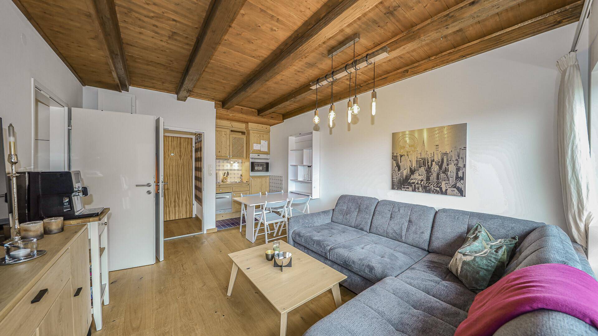 Heller Wohnbereich mit integrierter Küchenzeile, Holzbalkendecke und Zugang zum Flur.