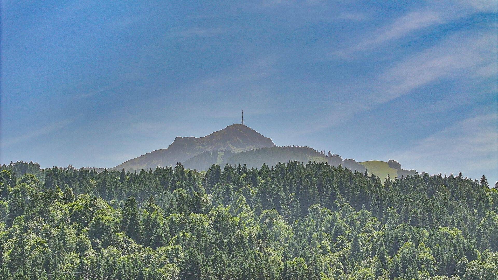 Panoramablick auf bewaldete Hügel und einen markanten Berggipfel mit Sendemast.