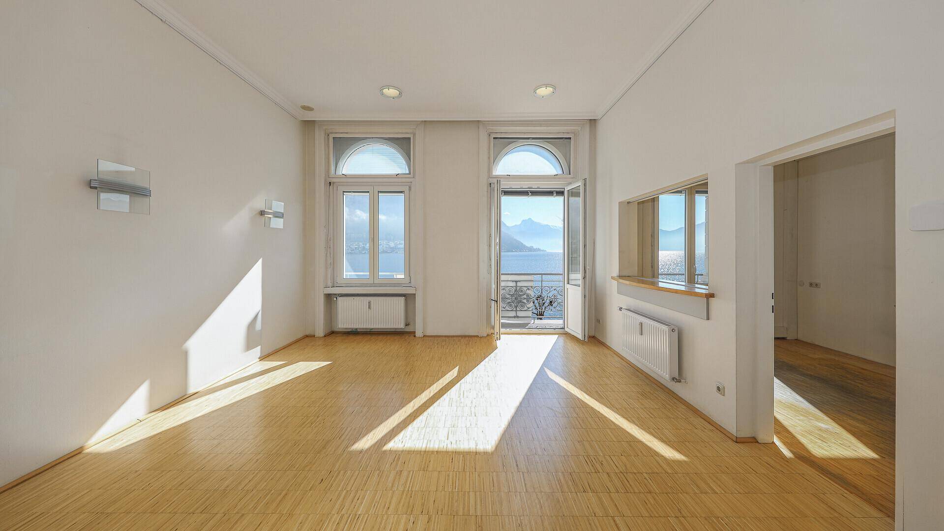 Heller Wohnraum mit Parkettboden, hohen Fenstern und Zugang zu einem französischen Balkon.