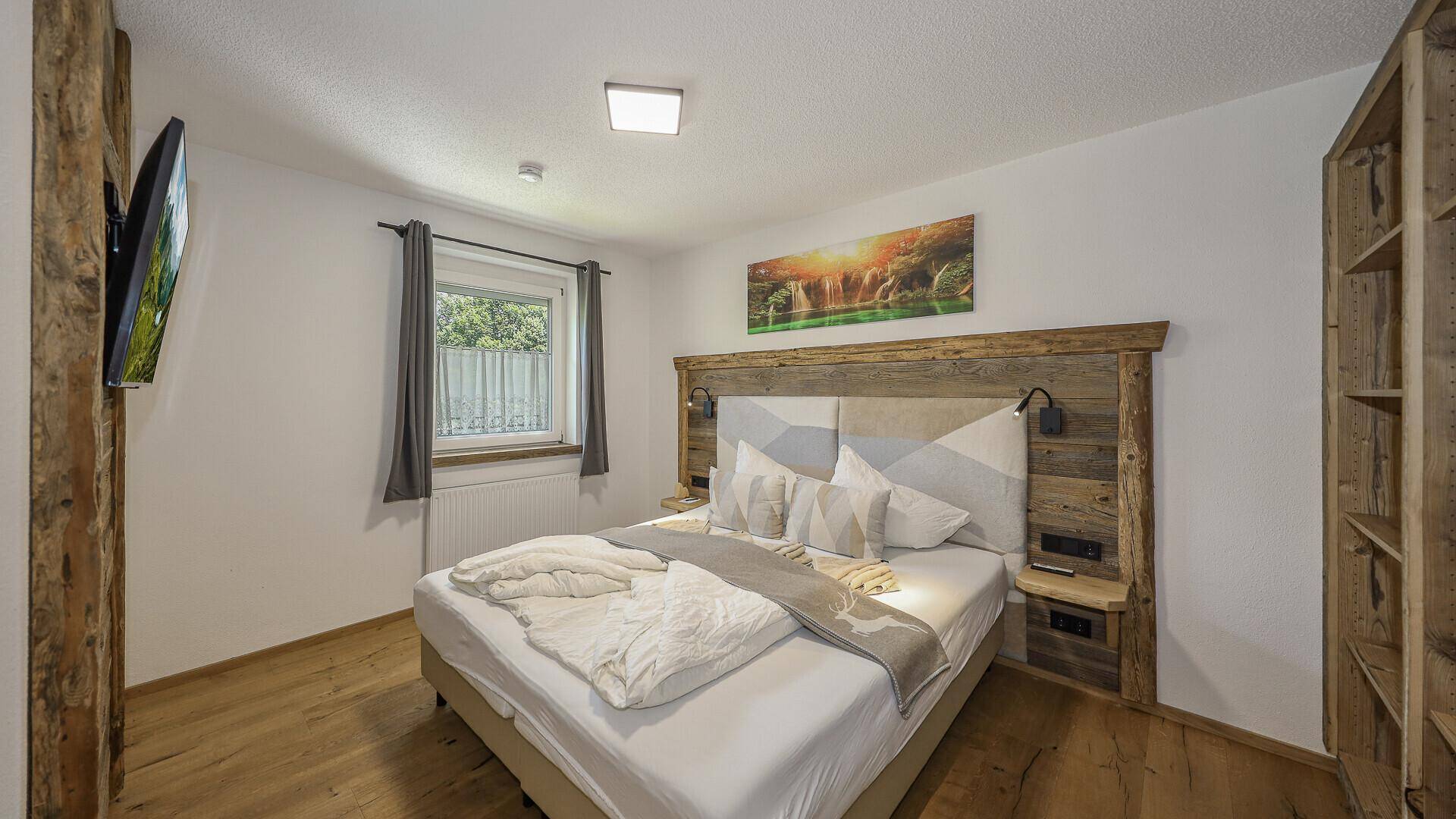 Helles Schlafzimmer mit Doppelbett, Holzboden und Fenster mit Blick ins Grüne.