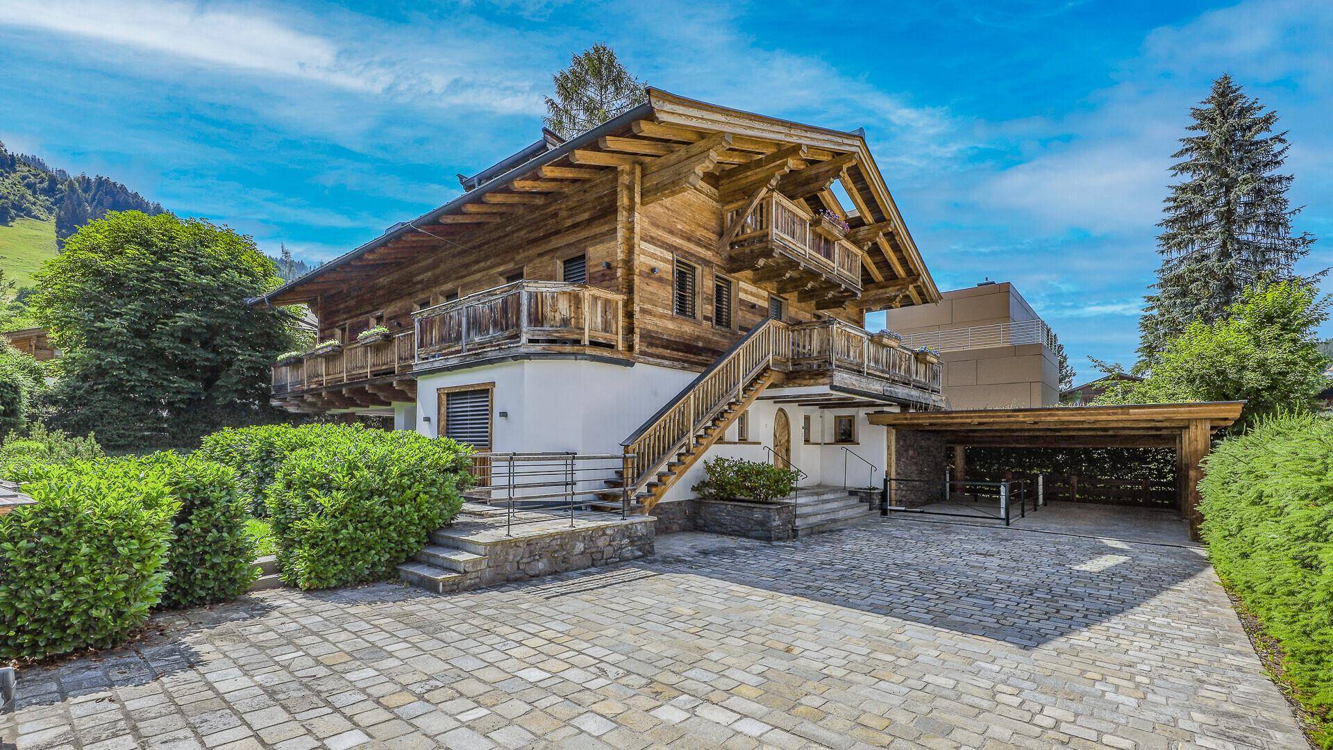 Traditionelles Holzchalet mit Steinpflaster-Einfahrt und grüner Umgebung unter blauem Himmel.