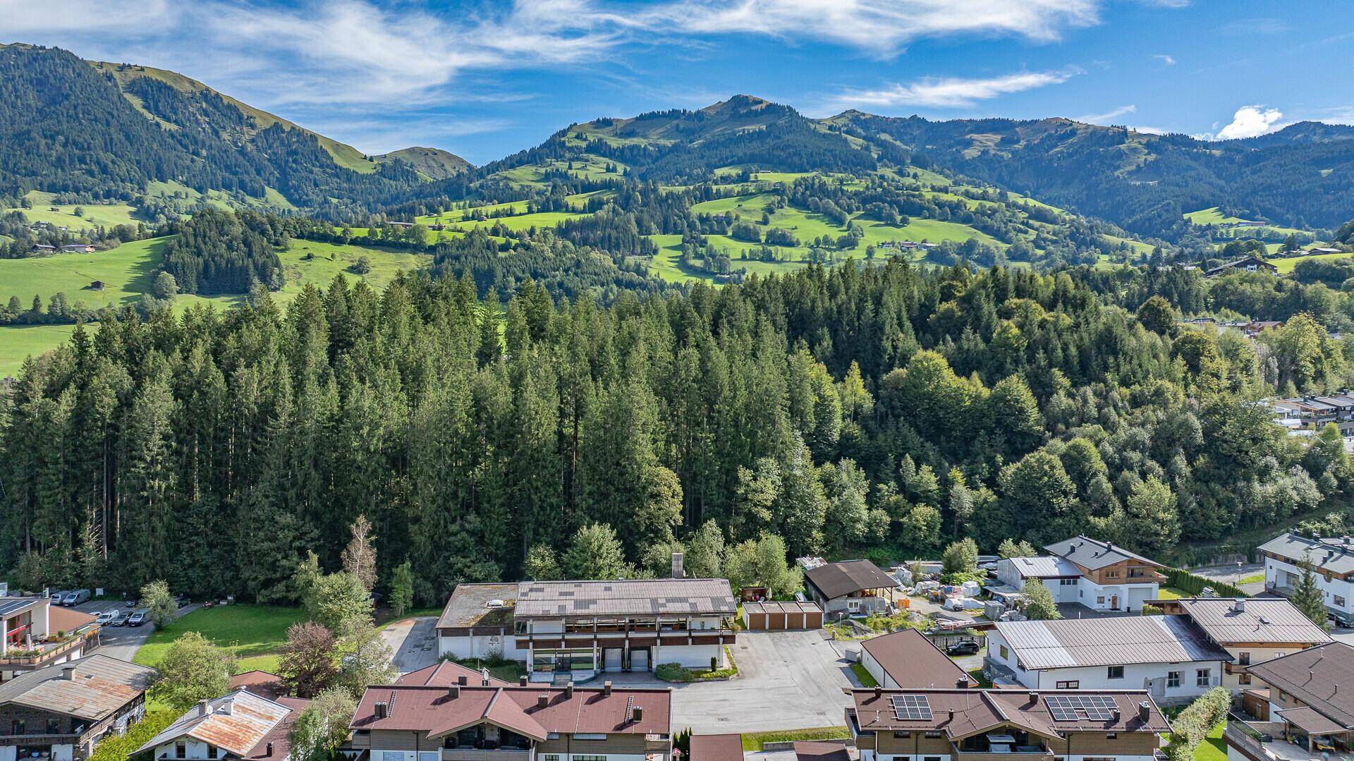 Übersicht des Anwesens aus der Vogelperspektive, eingebettet in eine grüne Hügellandschaft mit Wald.