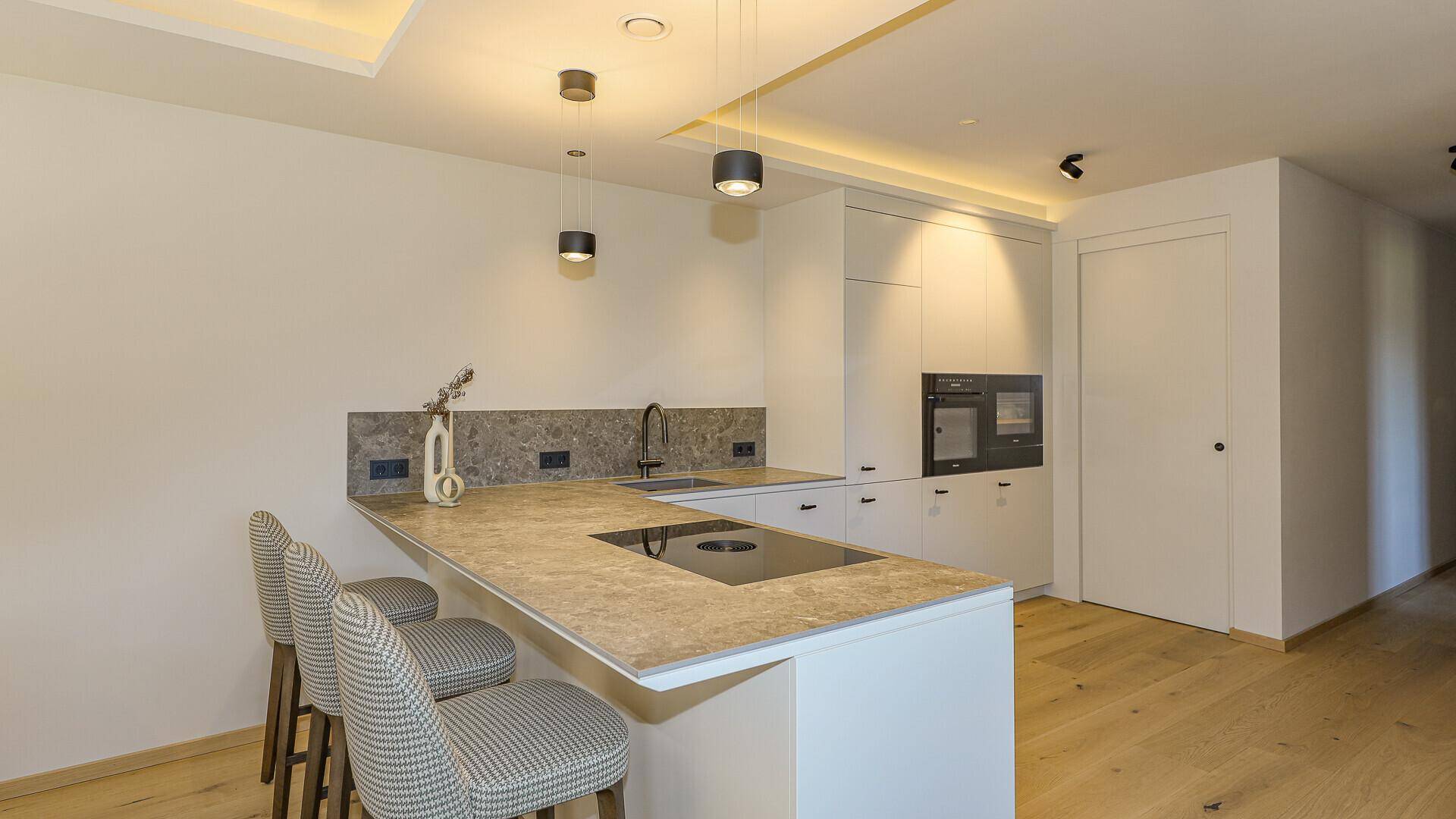 Elegante Küche mit Kochinsel, Induktionskochfeld und stilvollen Barhockern.