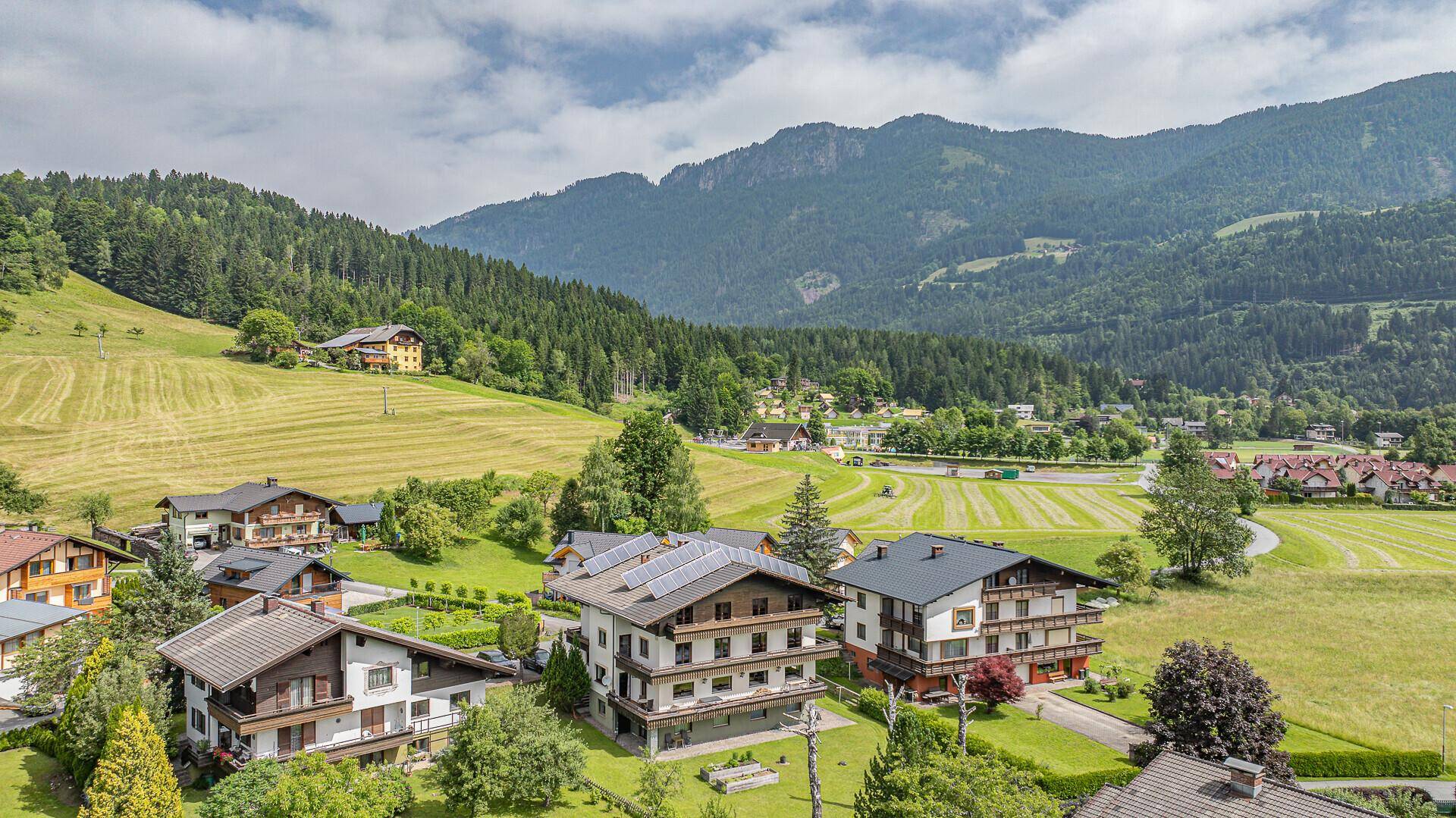Luftaufnahme eines malerischen Dorfes in den Bergen mit grünen Wiesen und traditionellen Häusern.