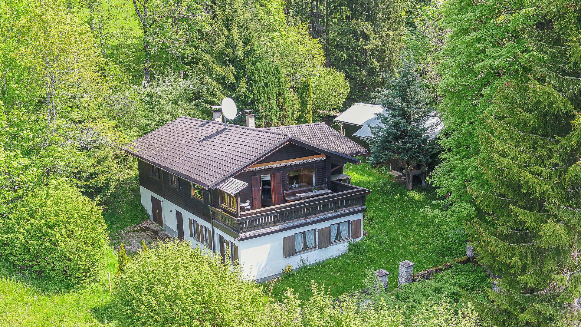 Traditionelles Holzchalet mit Balkon und Satteldach, umgeben von dichtem Wald und grüner Natur.