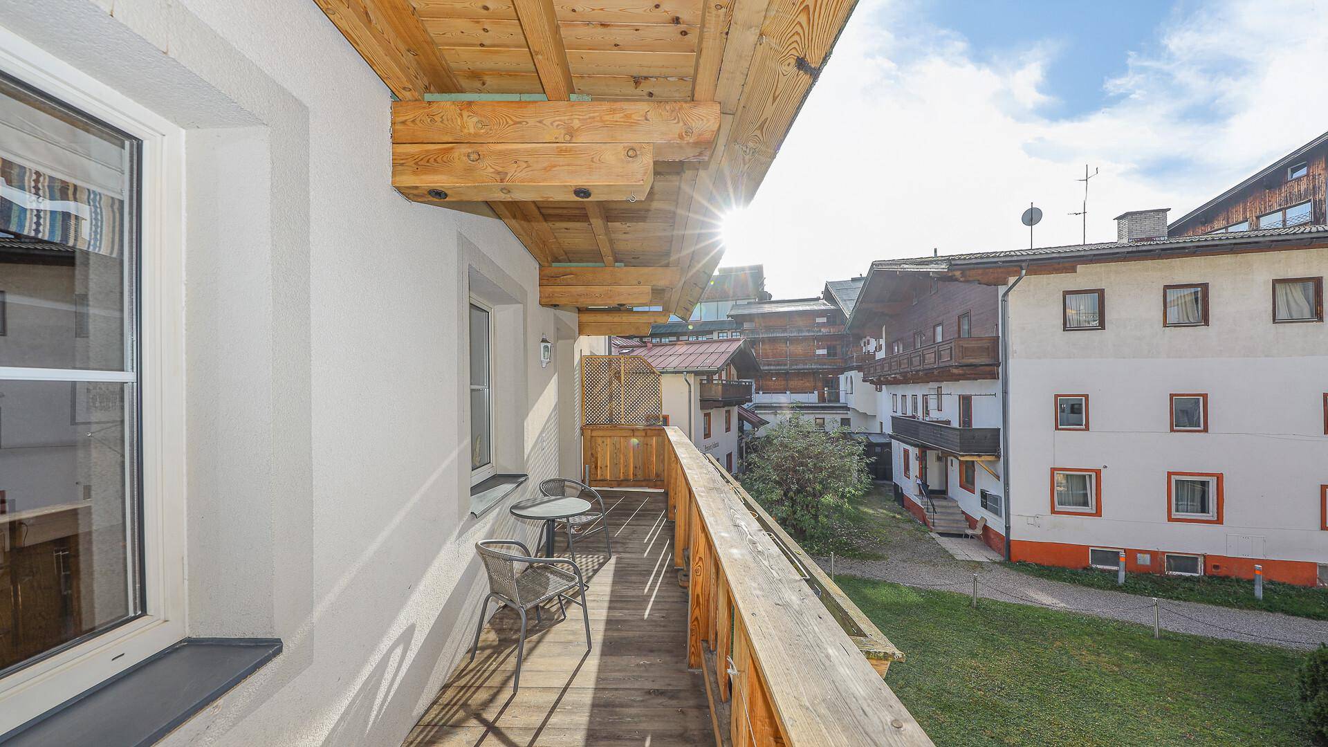Sonniger Balkon mit Holzboden und Sitzgelegenheiten, umgeben von anderen Gebäuden.