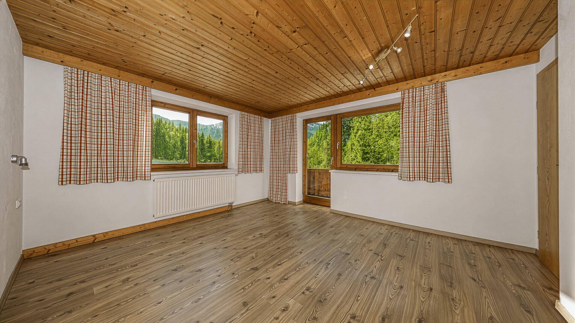 Heller Wohnraum mit Holzbalkendecke, Laminatboden und zwei Fenstern mit Bergblick.