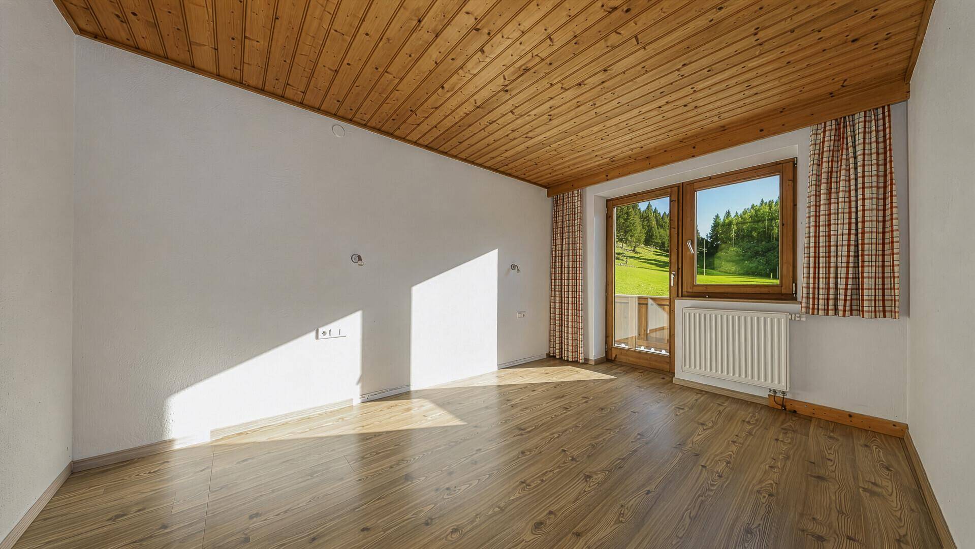 Helles Schlafzimmer mit Holzbalkendecke, Laminatboden und Zugang zum Balkon.