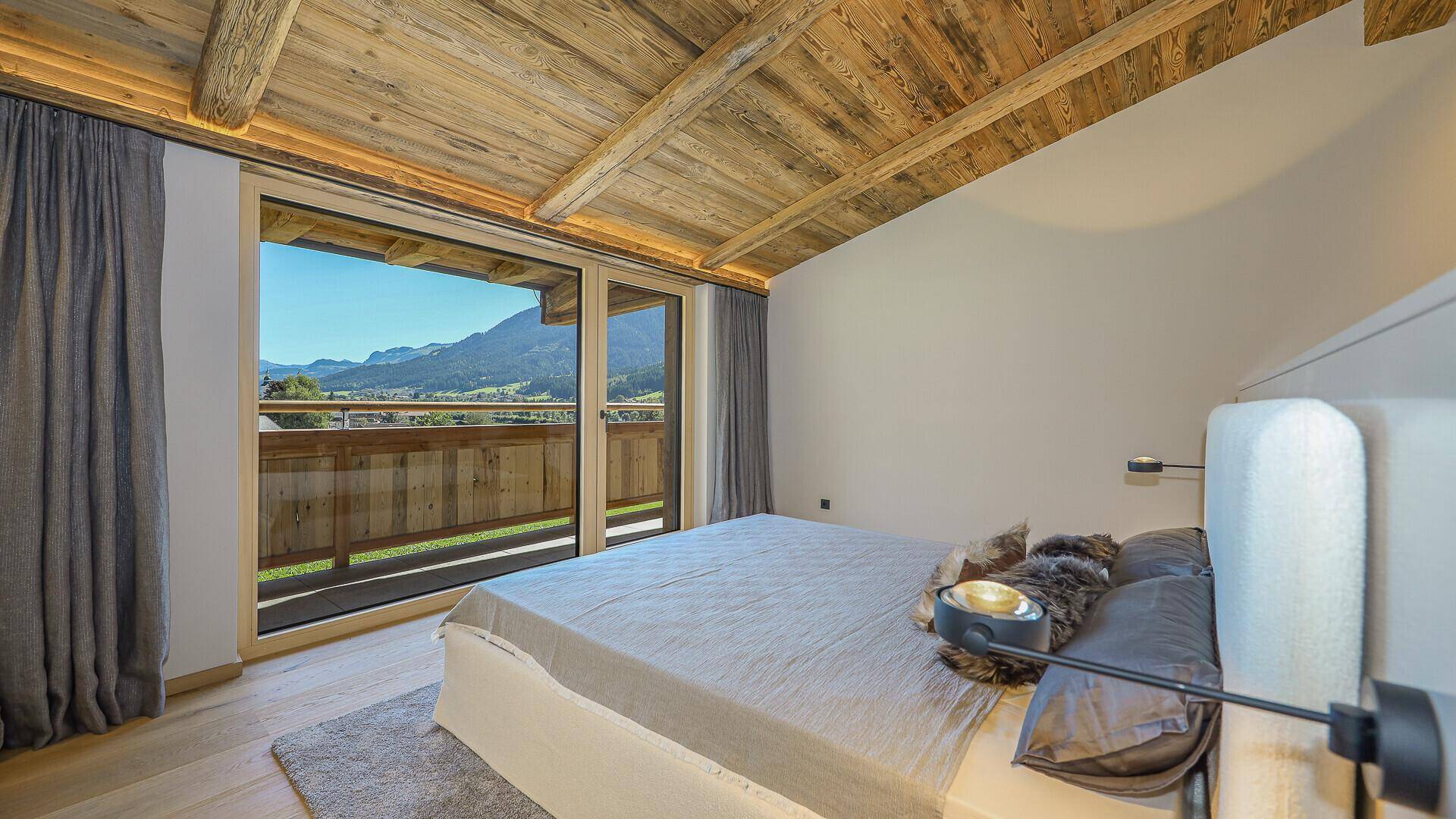 Helles Schlafzimmer mit Holzbalkendecke, großem Bett und Zugang zum Balkon mit Bergblick.