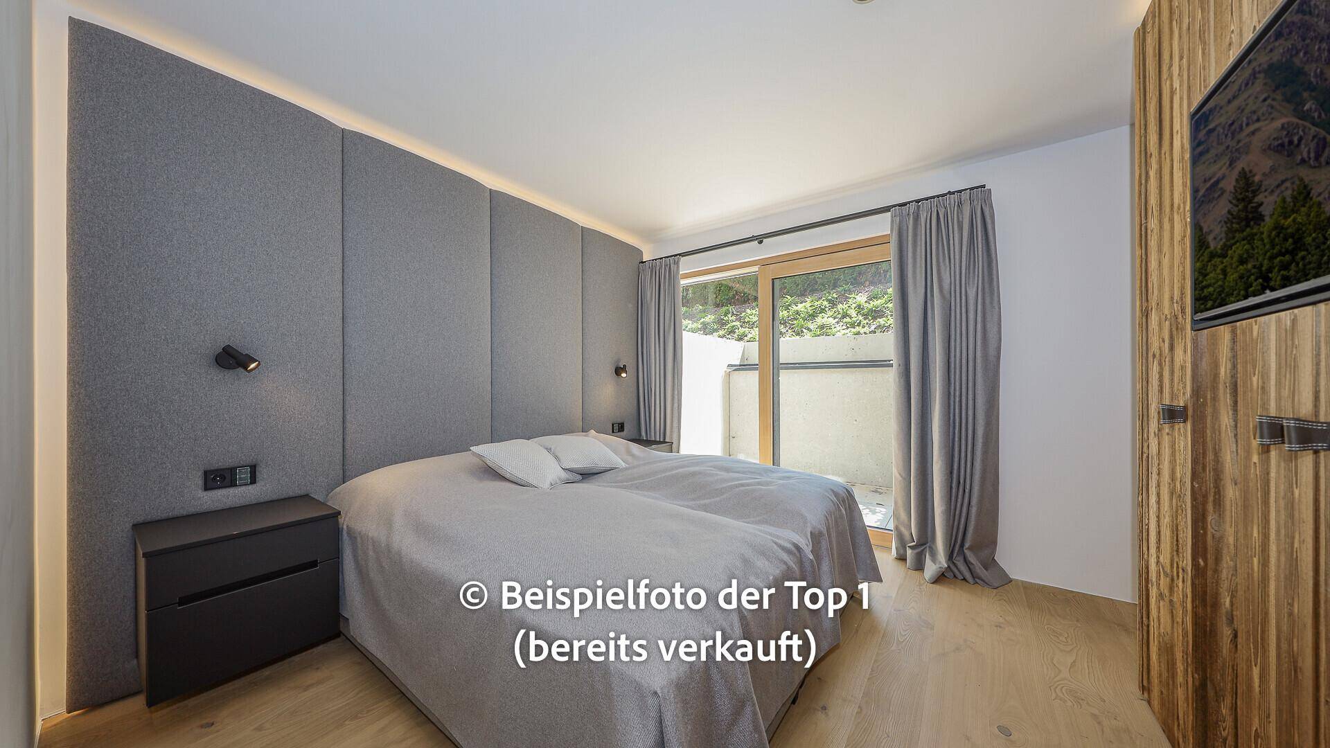 Helles Schlafzimmer mit großem Bett, gepolsterter Wand und Zugang zu einem Außenbereich.