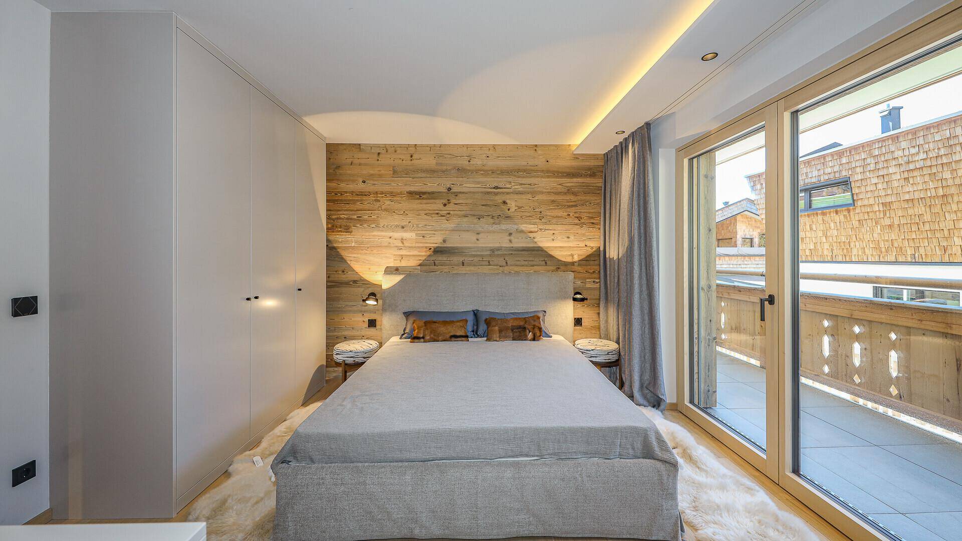 Gemütliches Schlafzimmer mit Holzwand, Doppelbett und Zugang zu einem Balkon.