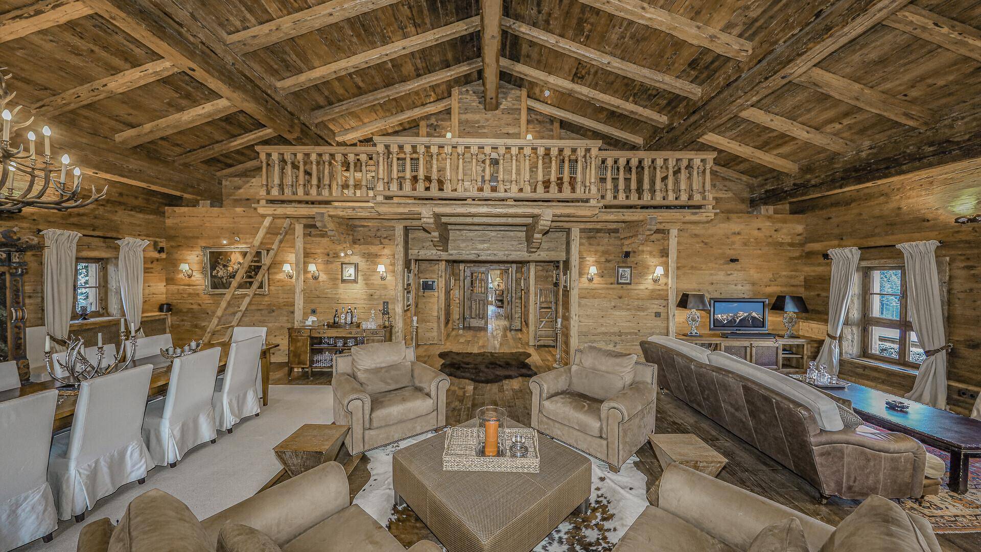 Geräumiger Wohnbereich im Chalet-Stil mit Holzbalkendecke, Galerie und großem Esstisch.