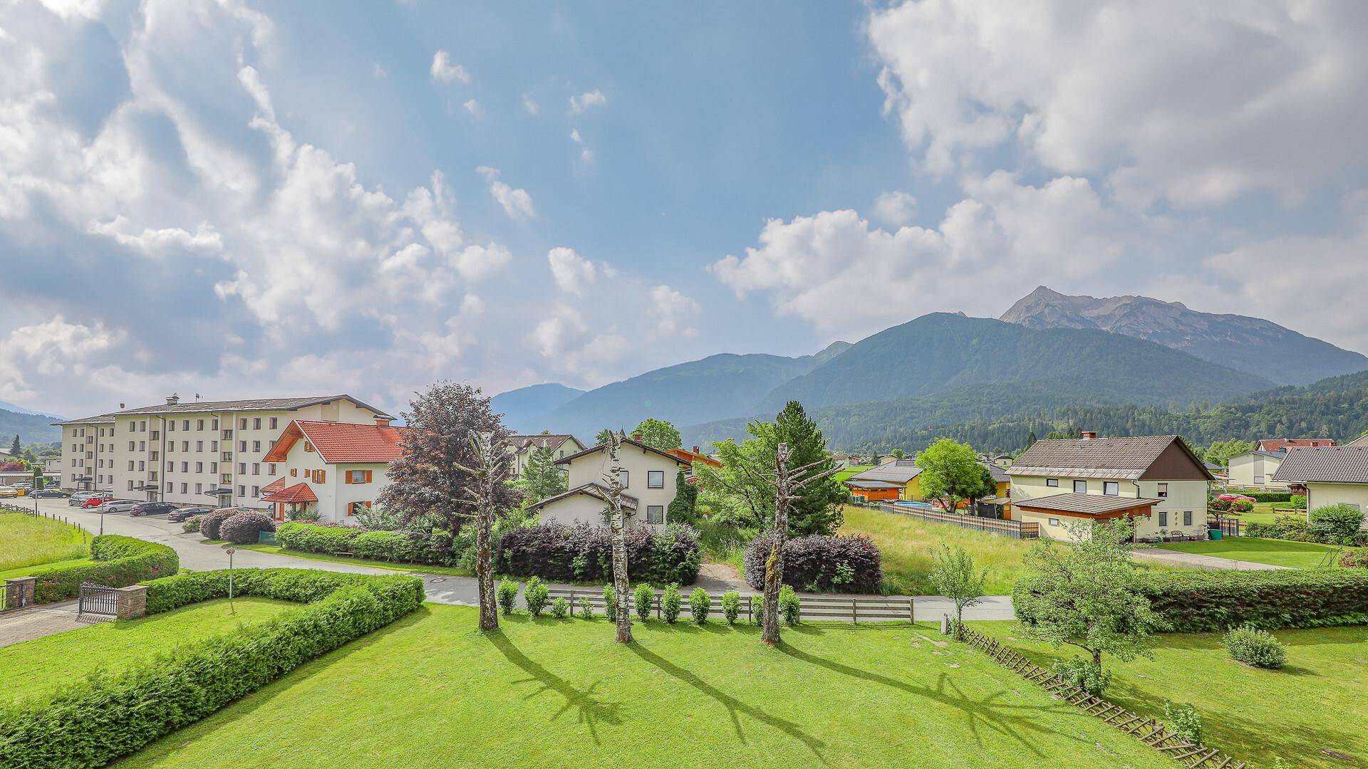 Weitläufiger Garten mit gepflegtem Rasen und Blick auf die umliegenden Häuser und die beeindruckende Berglandschaft.