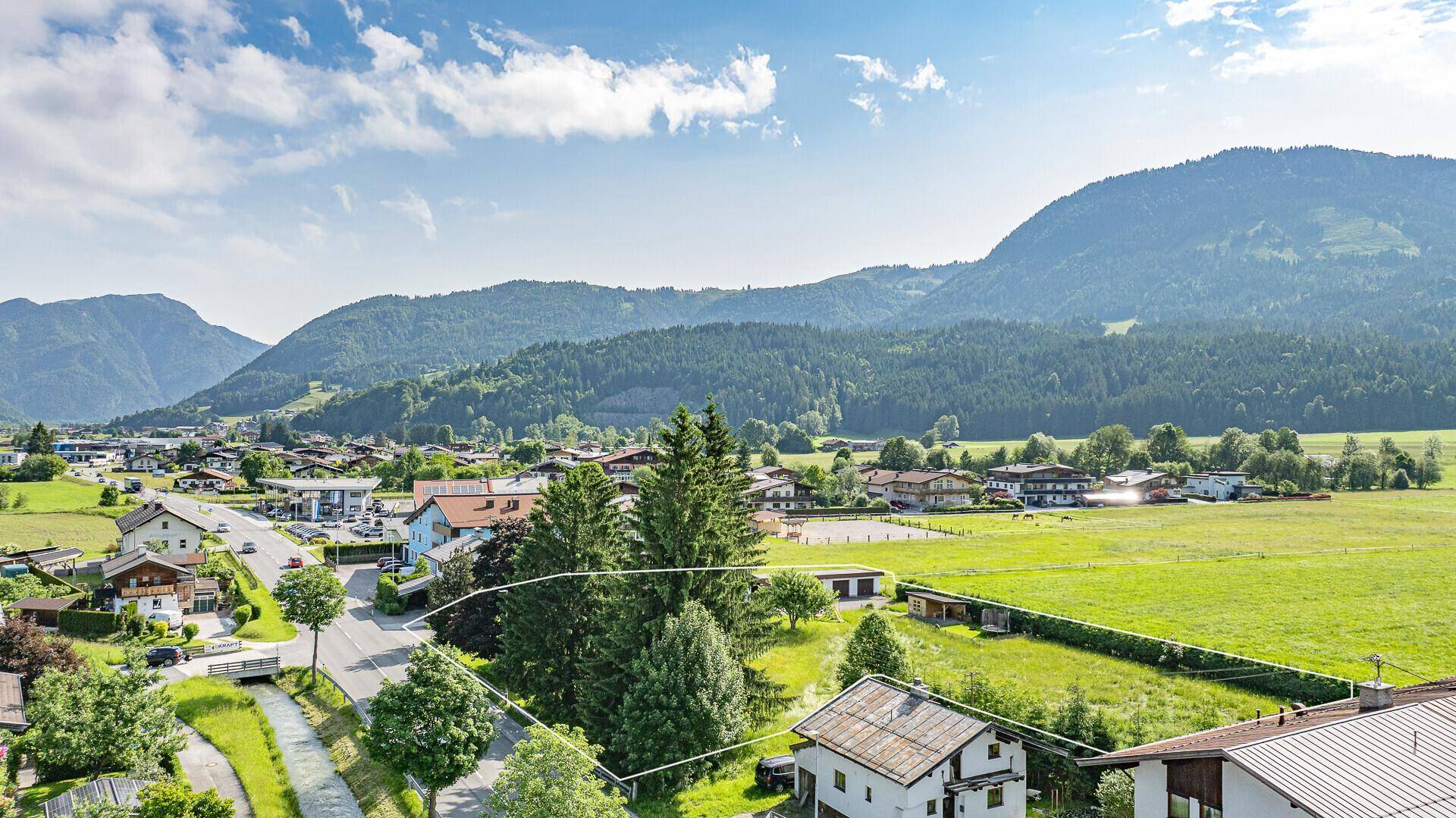 Luftaufnahme eines Grundstücks mit angrenzender Straße und weitem Blick auf die Bergwelt.