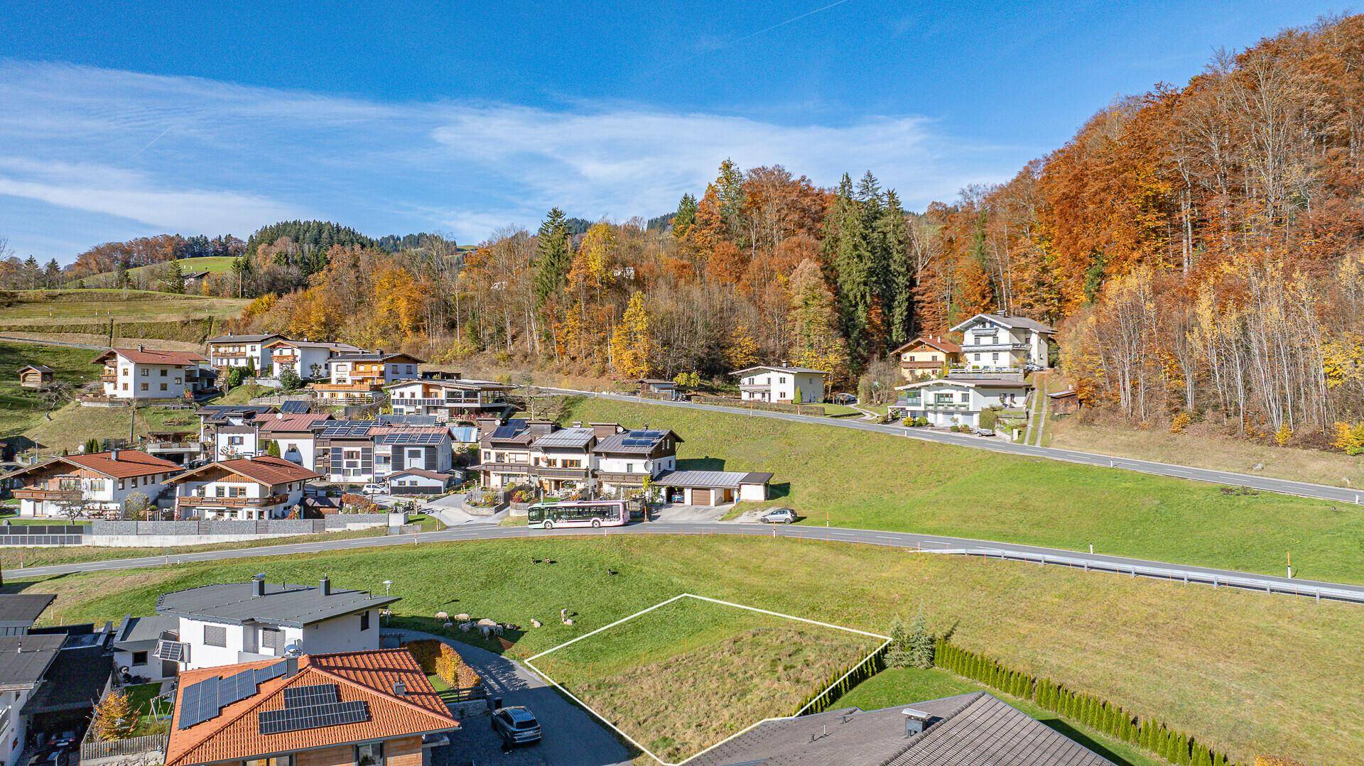 Luftaufnahme eines Baugrundstücks in einer malerischen Siedlung mit bewaldeten Hügeln.