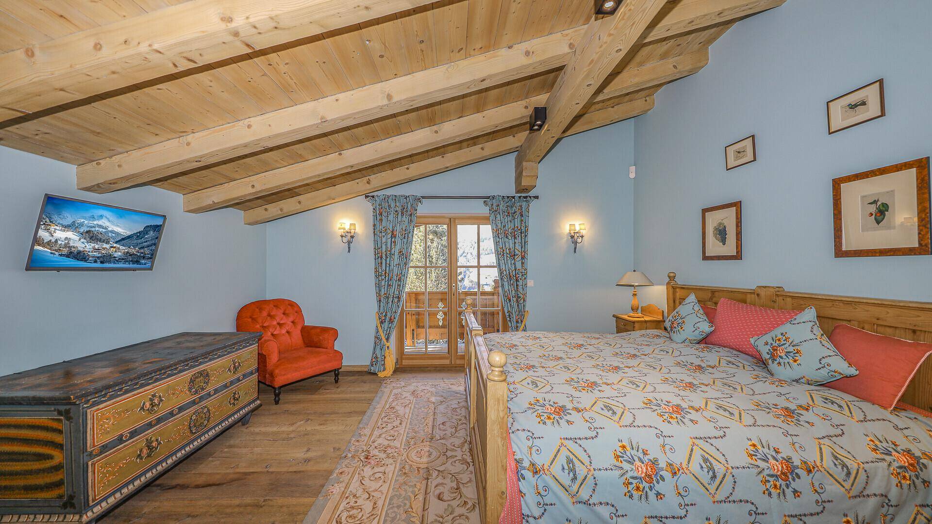 Geräumiges Schlafzimmer mit Holzbalkendecke, Balkonzugang und traditionellen Möbeln im alpinen Stil.