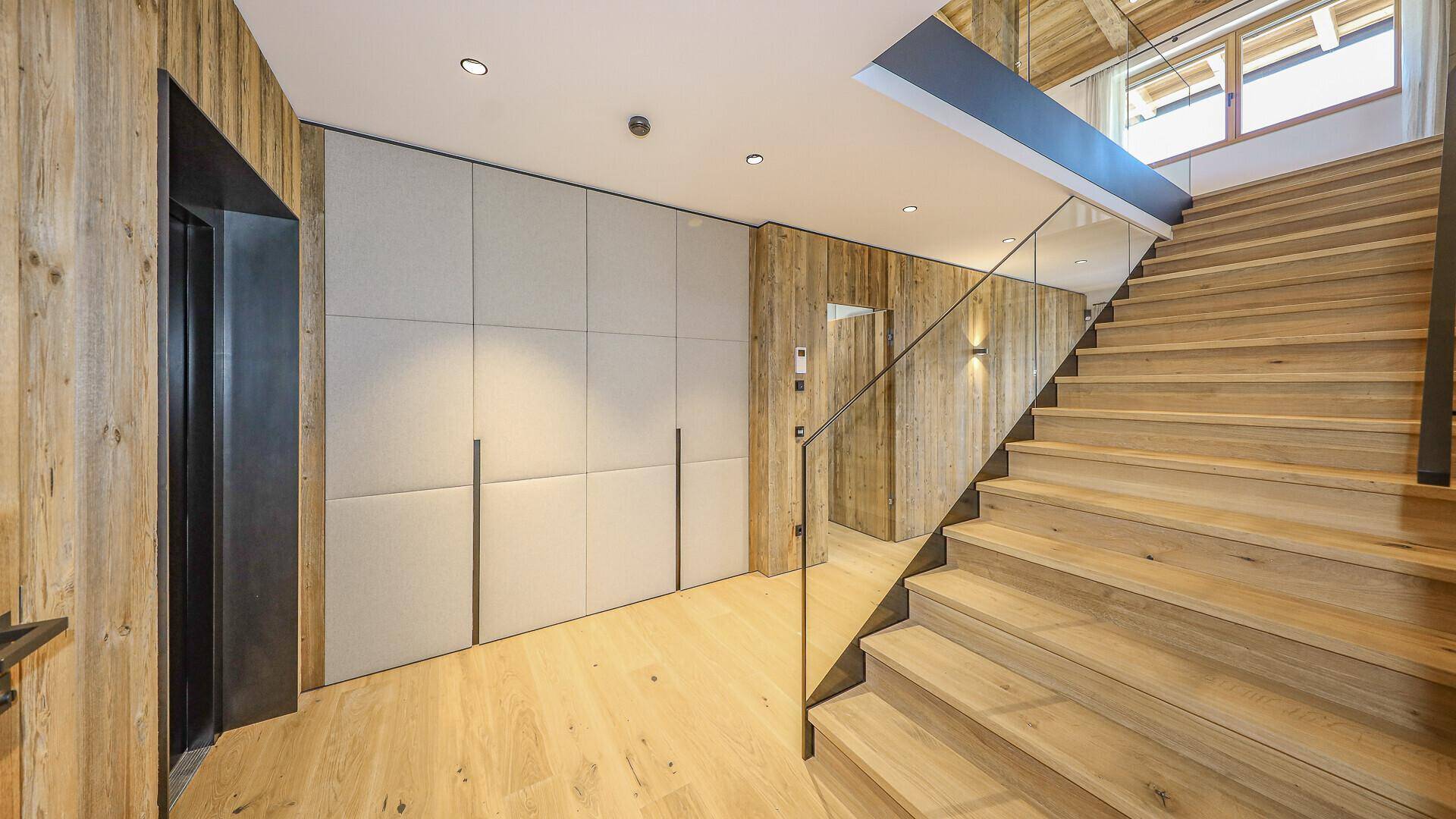 Geräumiger Flur mit Holztreppe, Glasgeländer und Aufzugzugang.