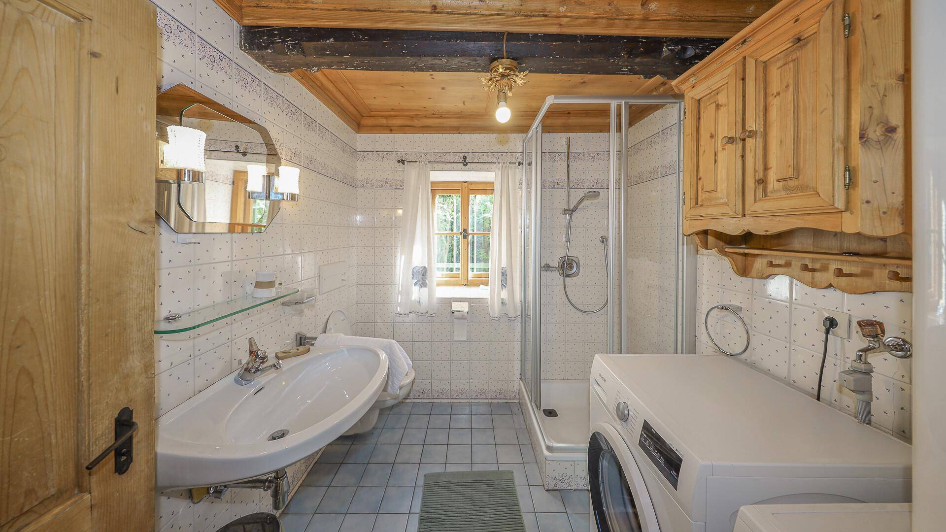Funktionales Badezimmer mit Dusche, Waschbecken und Waschmaschine, hell gefliest.