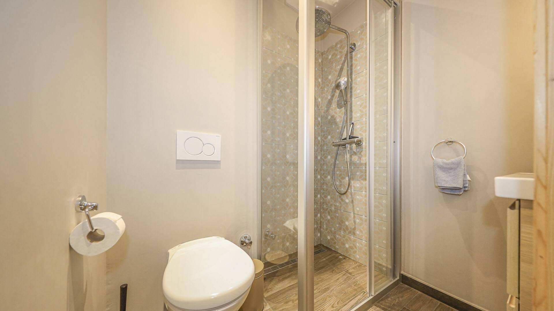 Modernes Badezimmer mit Duschkabine, WC und hellen Fliesen.
