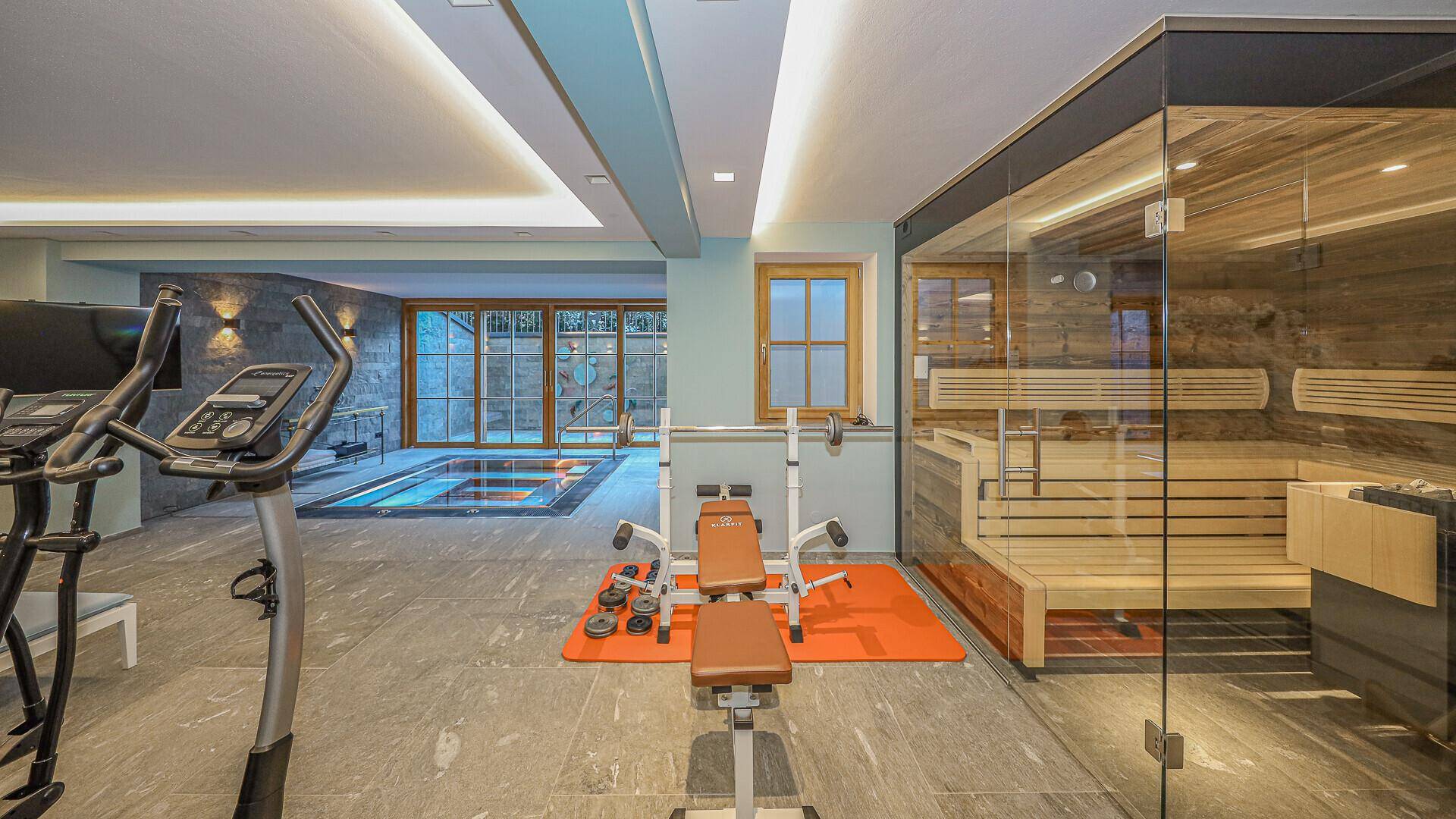 Exklusiver Wellnessbereich mit Sauna, Fitnessgeräten und Blick auf den Whirlpool.