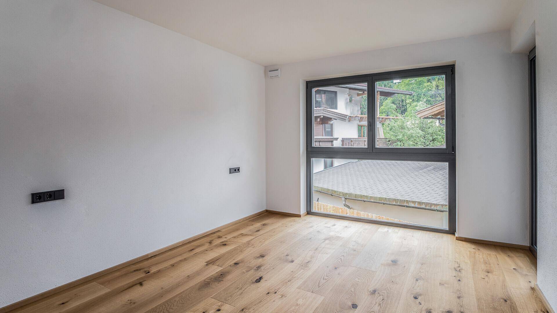 Helles Schlafzimmer mit Holzboden und großem Fenster, das viel Tageslicht hereinlässt.