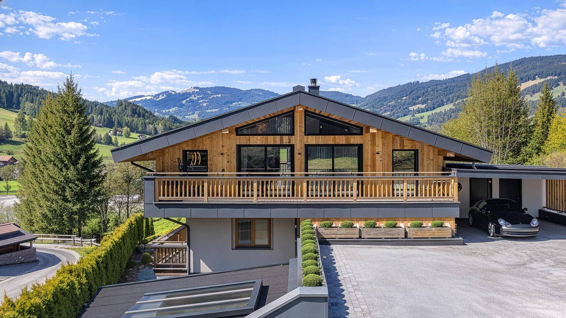 Modernes Chalet mit Holzfassade, Carport und gepflegter Außenanlage in den Bergen.