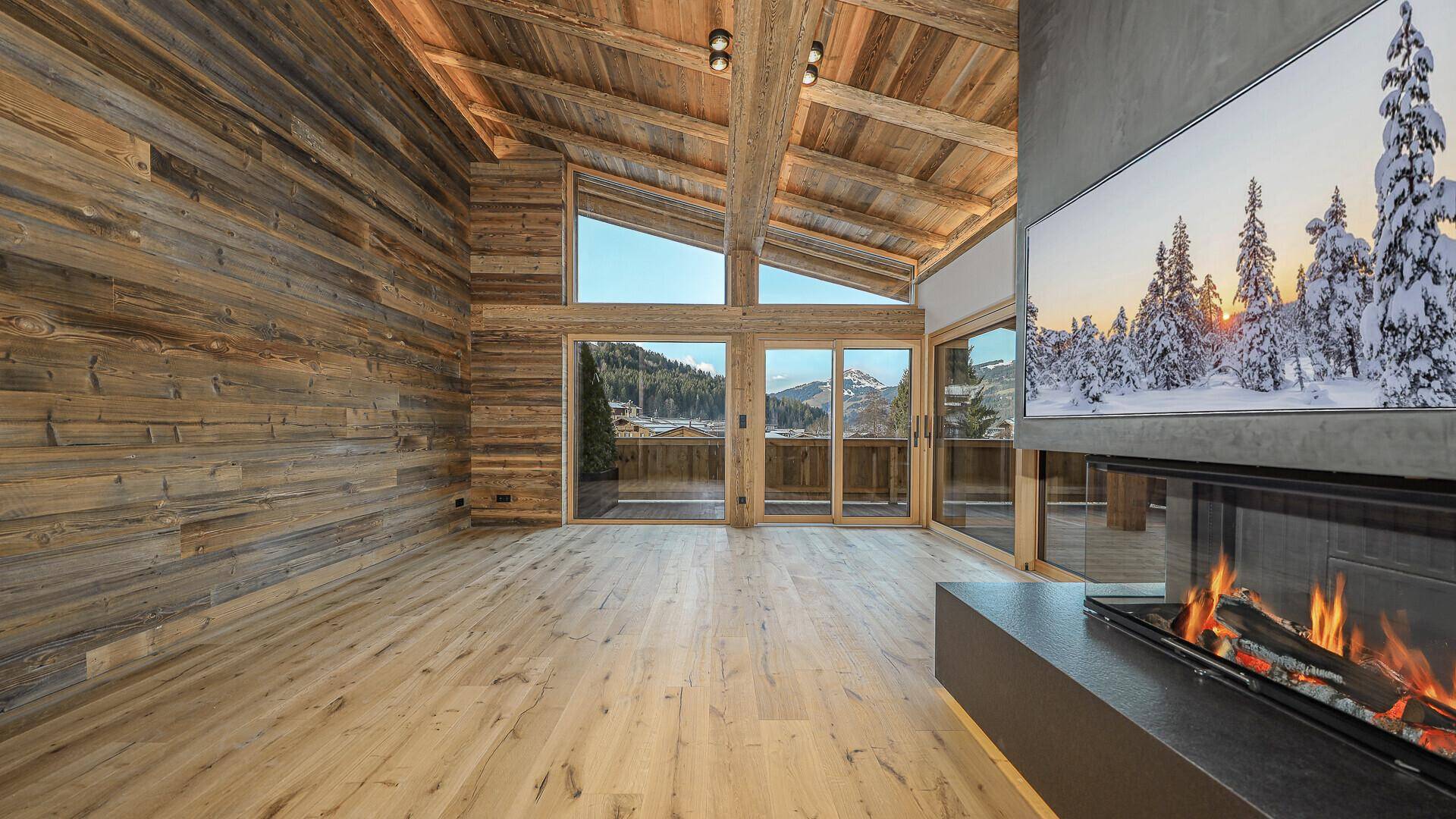 Gemütliches Wohnzimmer mit modernem Kamin, Holzwänden und weitem Blick auf die umliegende Berglandschaft.
