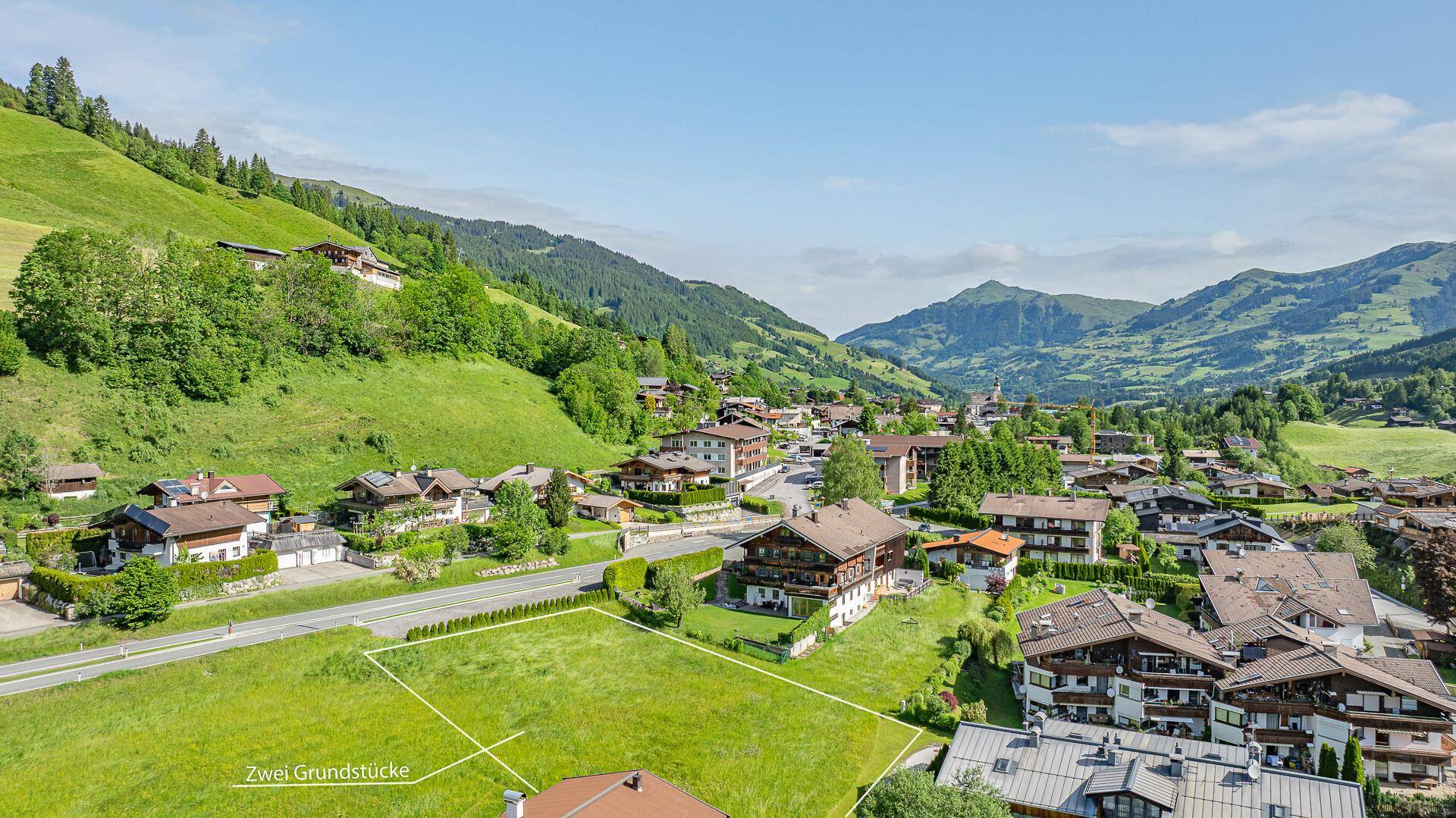 Luftaufnahme eines Dorfes in den Bergen mit zwei markierten Grundstücken und grünen Wiesen.