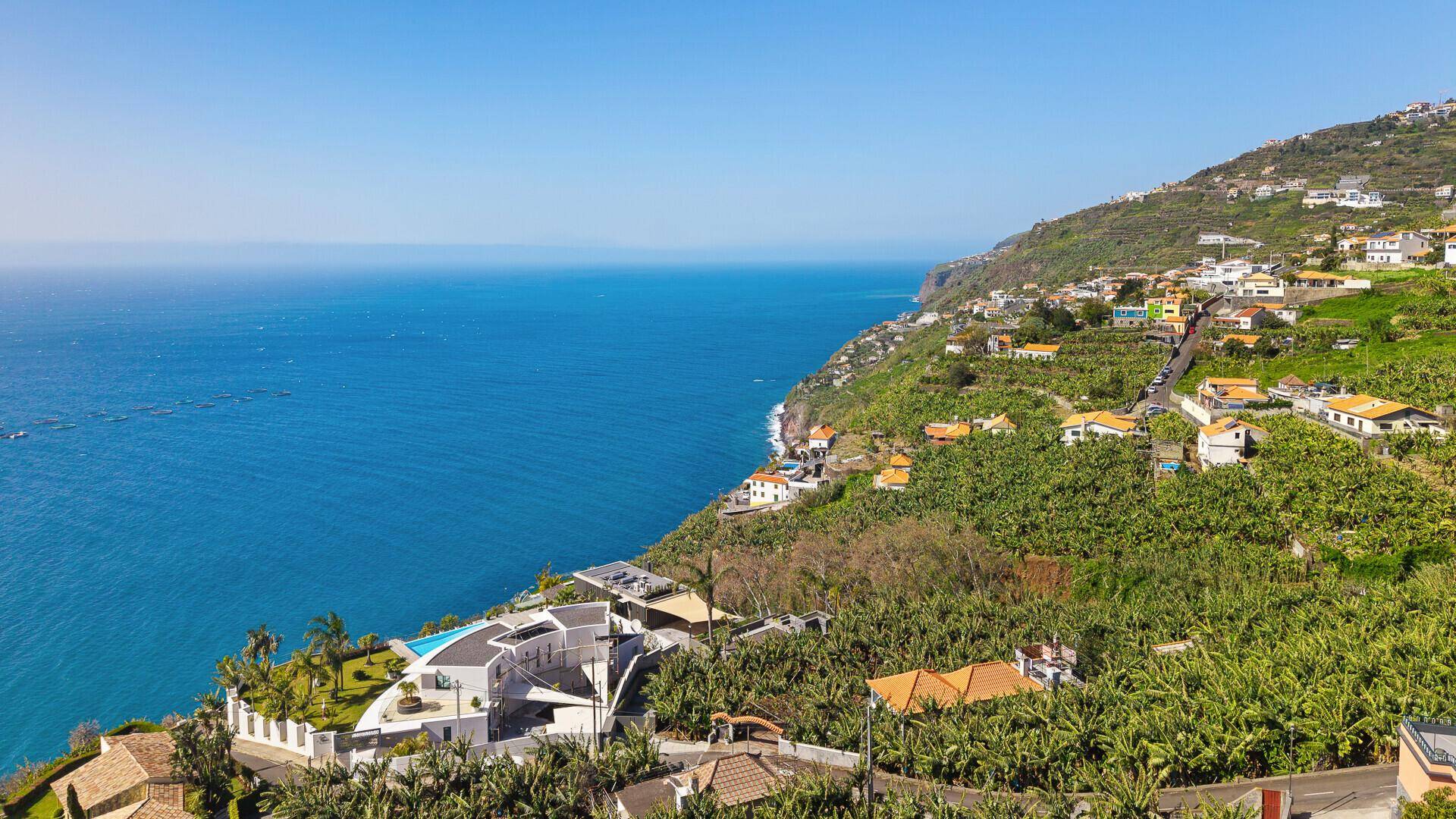Atemberaubende Küstenlandschaft mit luxuriöser Villa auf einer Klippe, umgeben von Bananenplantagen und dem weiten Meer.