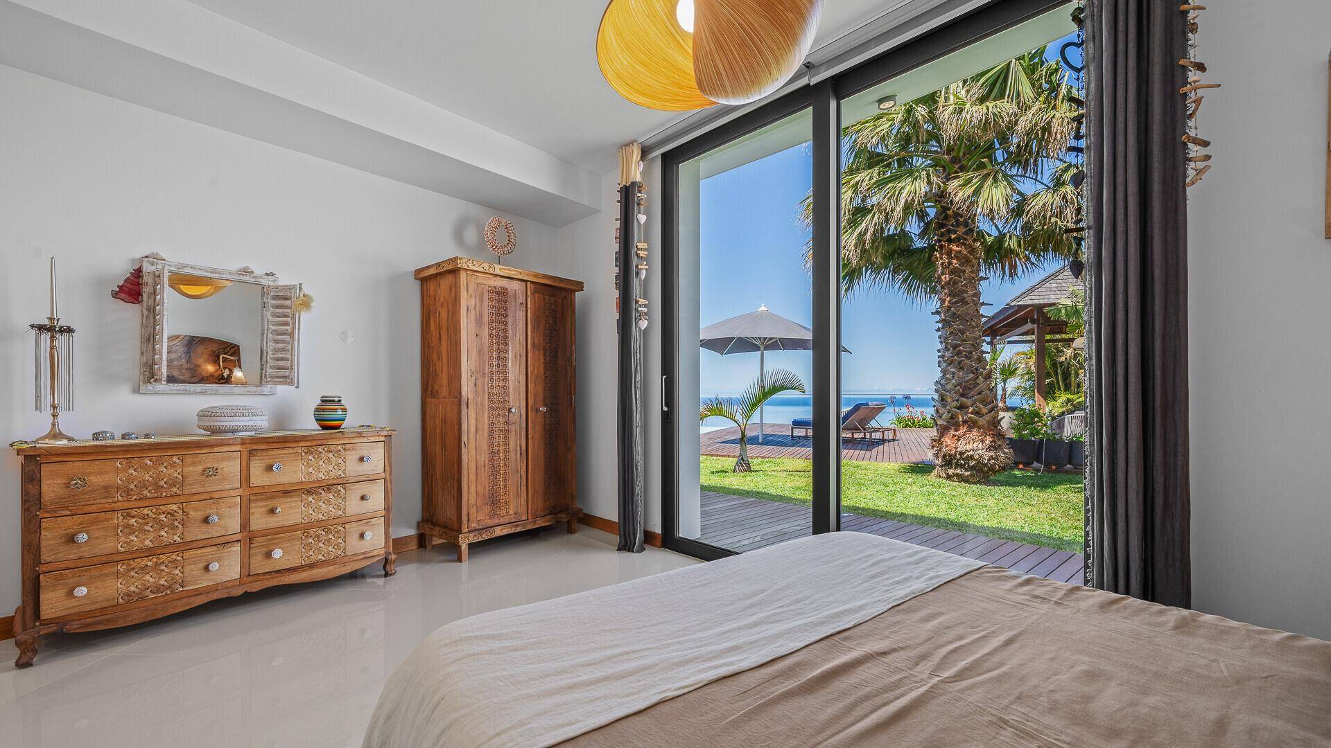 Schlafzimmer mit Holzelementen, Meerblick und direktem Zugang zum gepflegten Gartenbereich.