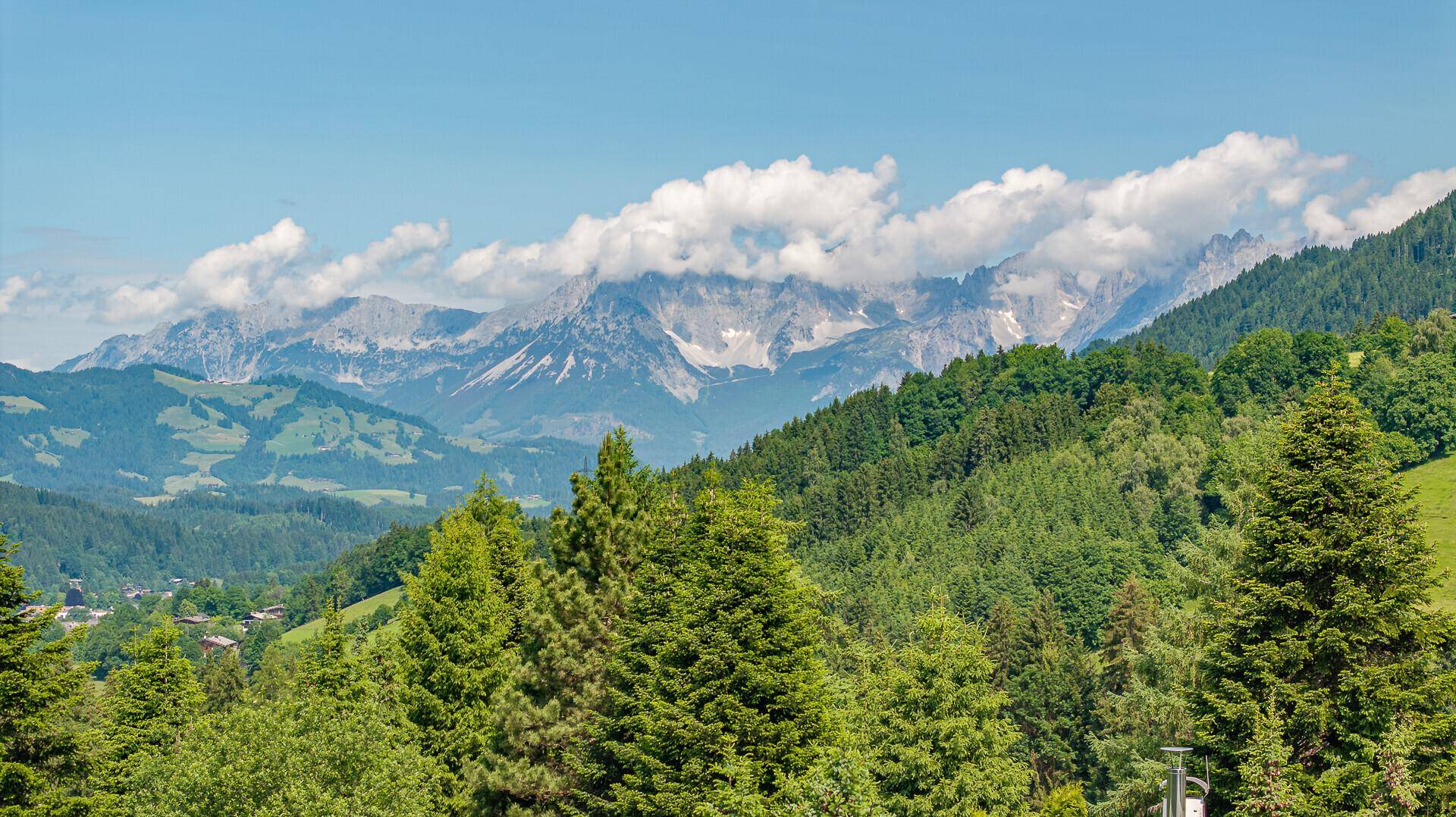 Spektakulärer Panoramablick auf die majestätischen Alpen mit bewaldeten Hängen und Wolken.