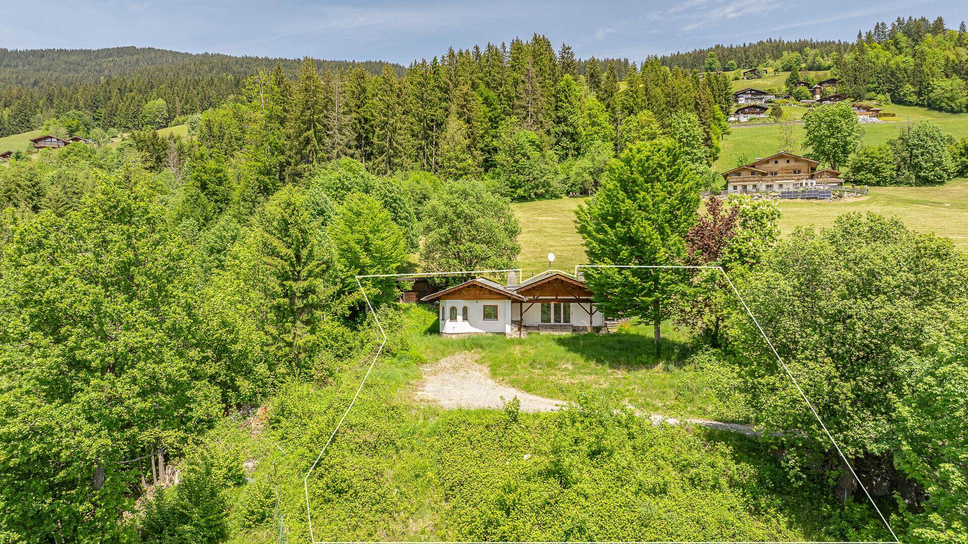 Luftaufnahme eines kleinen Hauses umgeben von Bäumen und Wiesen mit Bergblick.