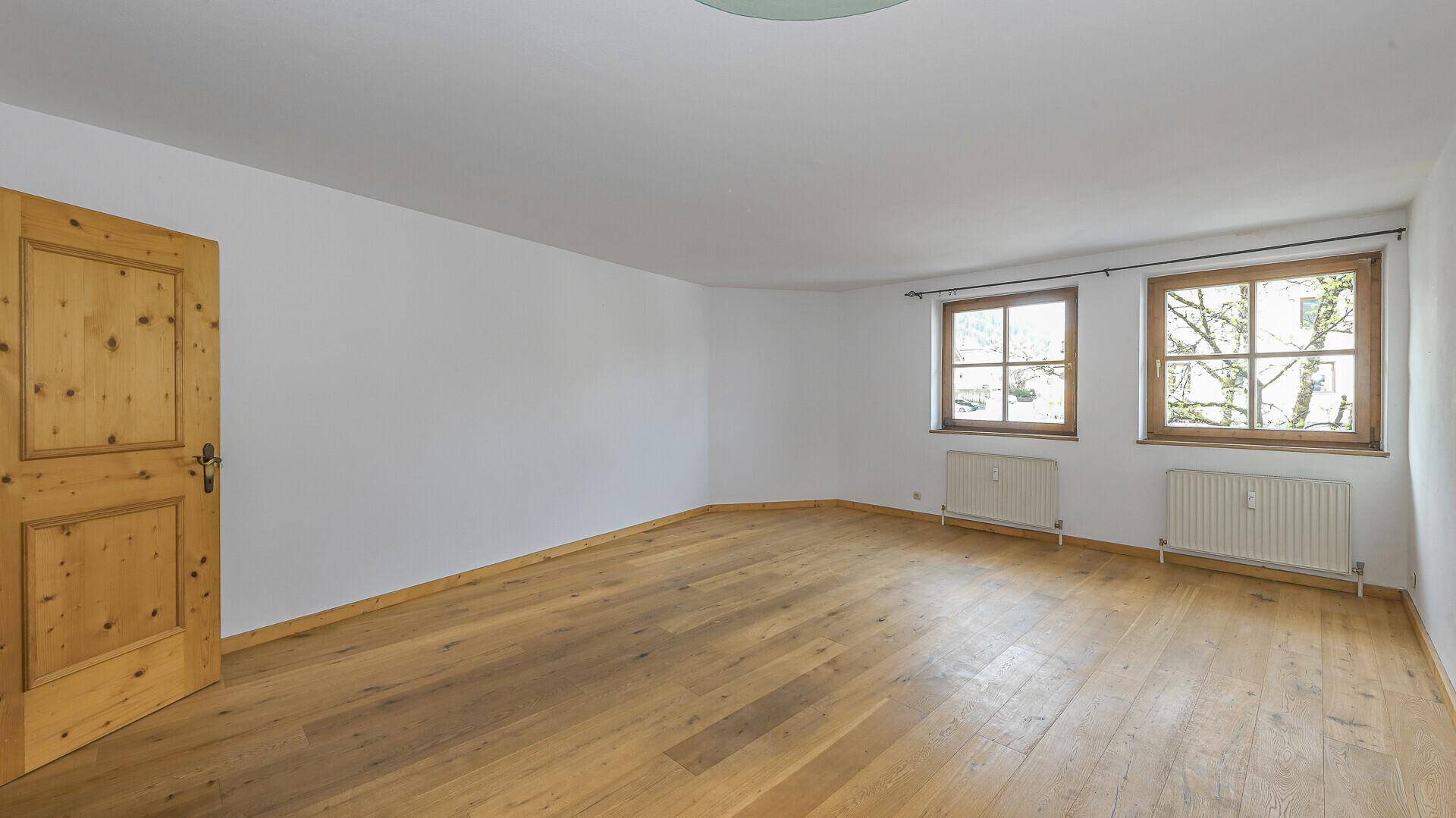 Leeres Zimmer mit Holzboden und Holztür, bietet viel Potenzial für individuelle Einrichtungsideen.
