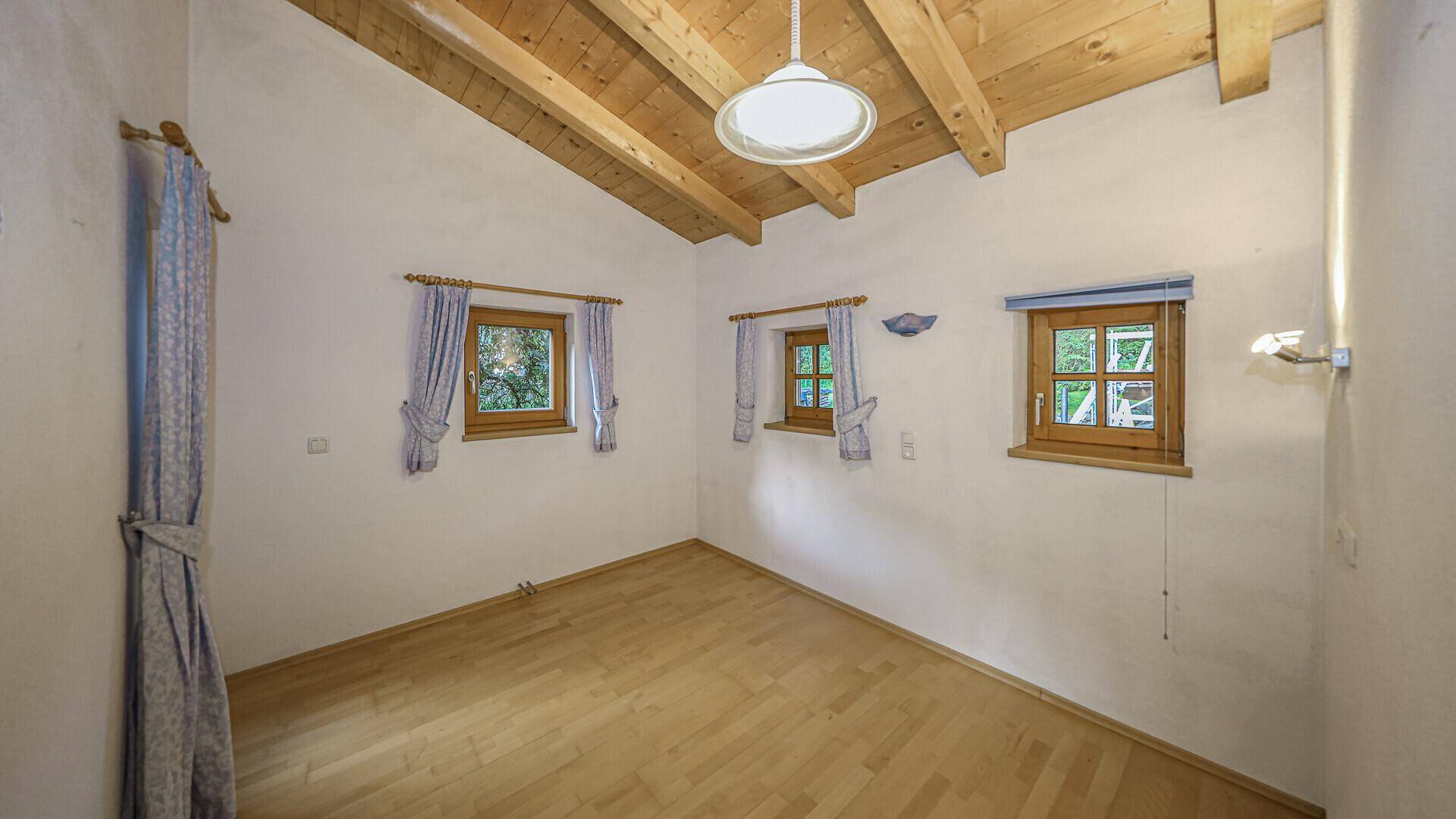 Helles Schlafzimmer mit Holzboden, mehreren Fenstern und Vorhängen im Landhausstil.