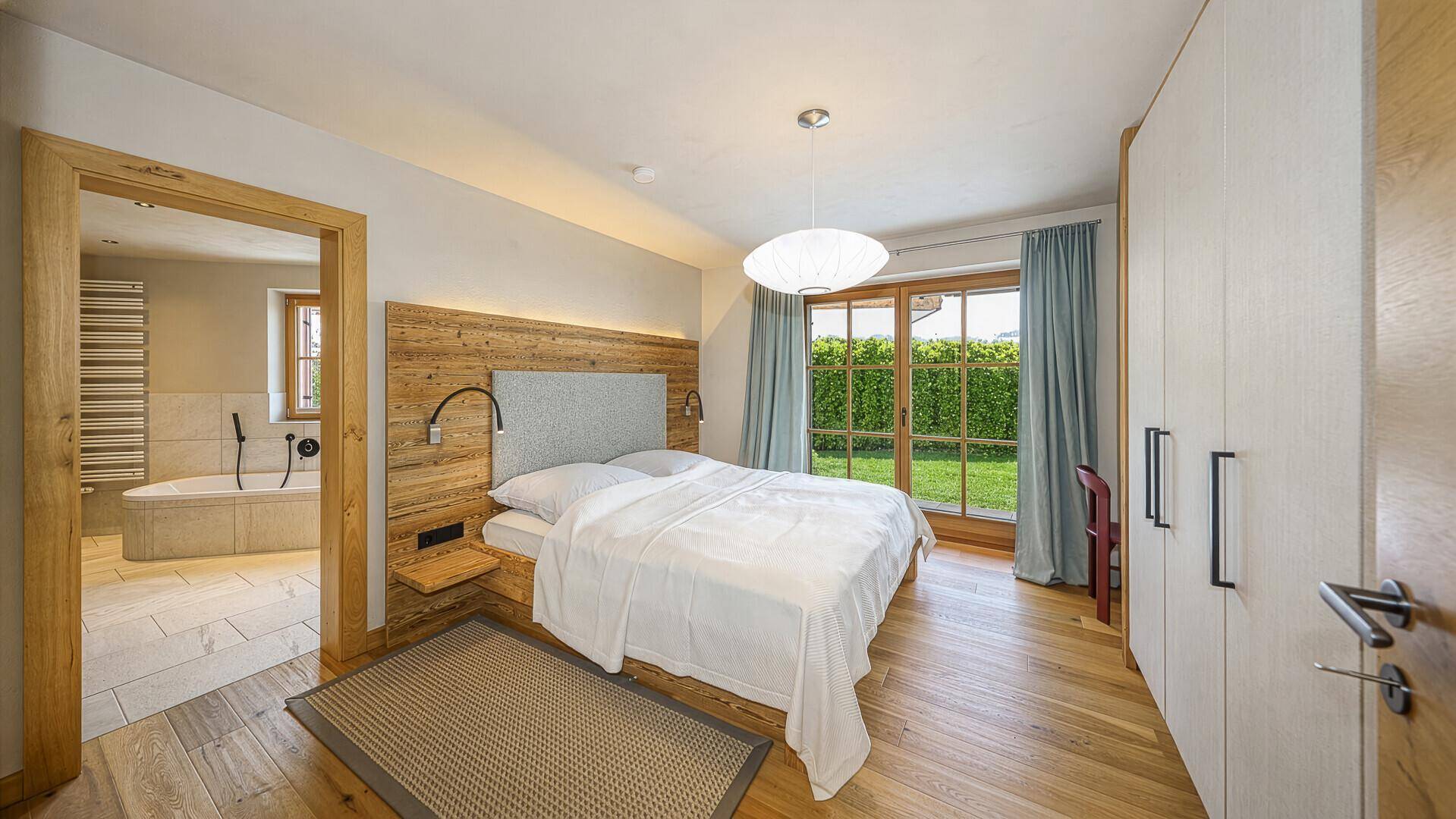 Helles Schlafzimmer mit Holzboden, Doppelbett und Zugang zu einem angrenzenden Badezimmer.