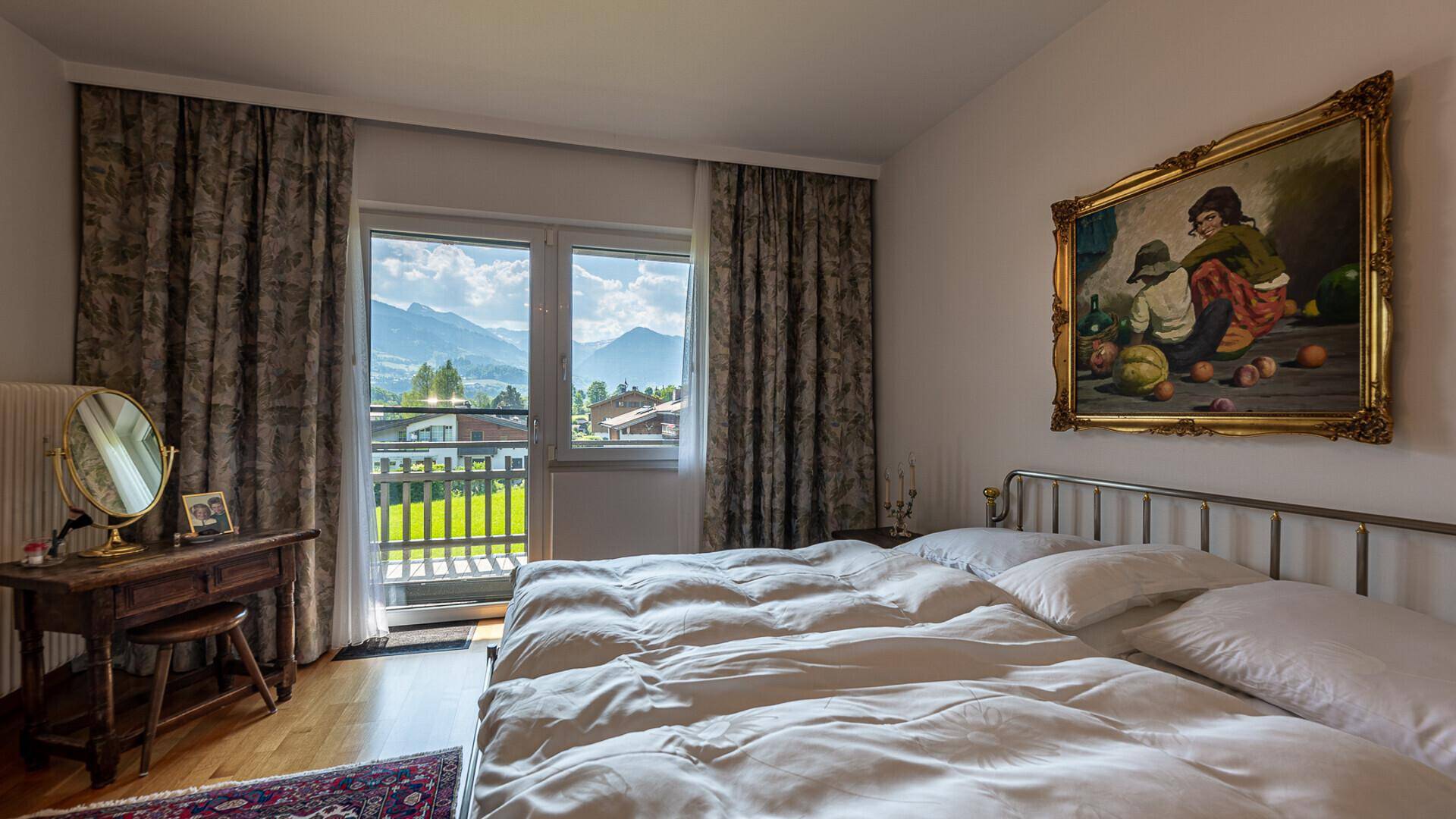 Schlafzimmer mit Doppelbett, traditionellem Schminktisch und Balkonzugang mit Bergblick.