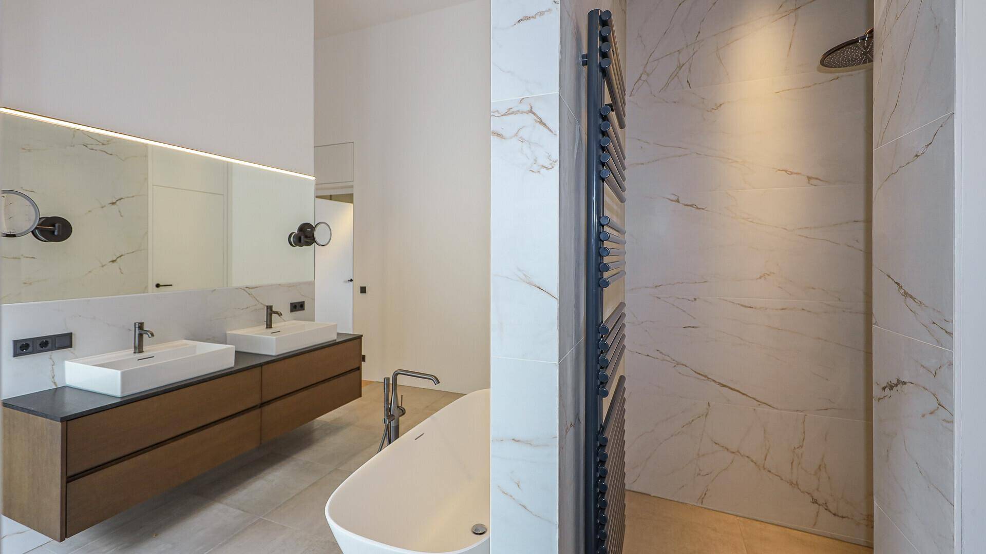 Stilvolles Badezimmer mit Doppelwaschbecken, beheiztem Handtuchhalter und großer Dusche.